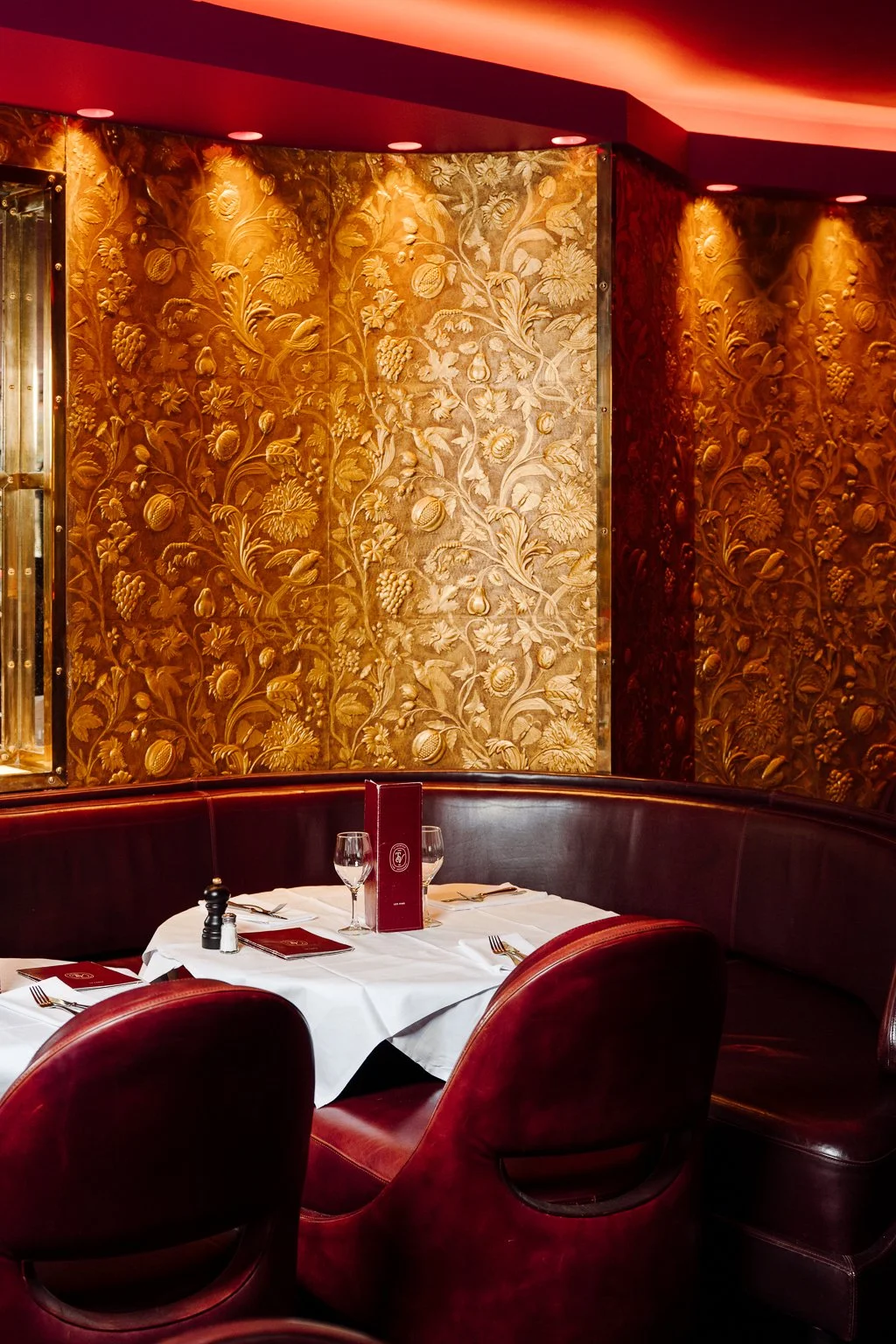 Tables à manger dans un restaurant élégant avec assiettes, couverts, verres à vin, nappe blanche, chaises en cuir brun, et décor sombre au restaurant Le Tourville Paris 7ème.