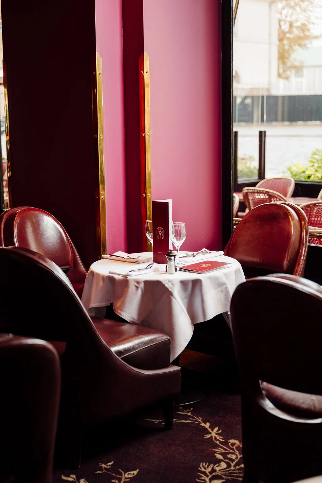 Tables à manger dans un restaurant élégant avec assiettes, couverts, verres à vin, nappe blanche, chaises en cuir brun, et décor sombre au restaurant Le Tourville Paris 7ème.