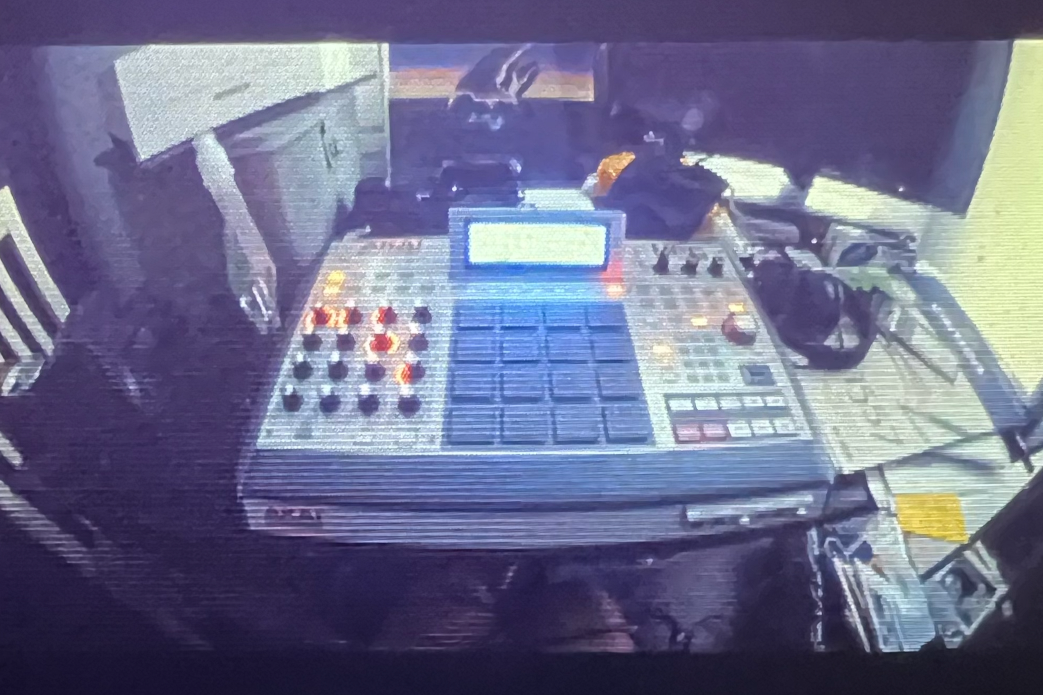 DJ or music production equipment with a laptop, mixer, headphones and various cables on a desk, in a dimly lit room.