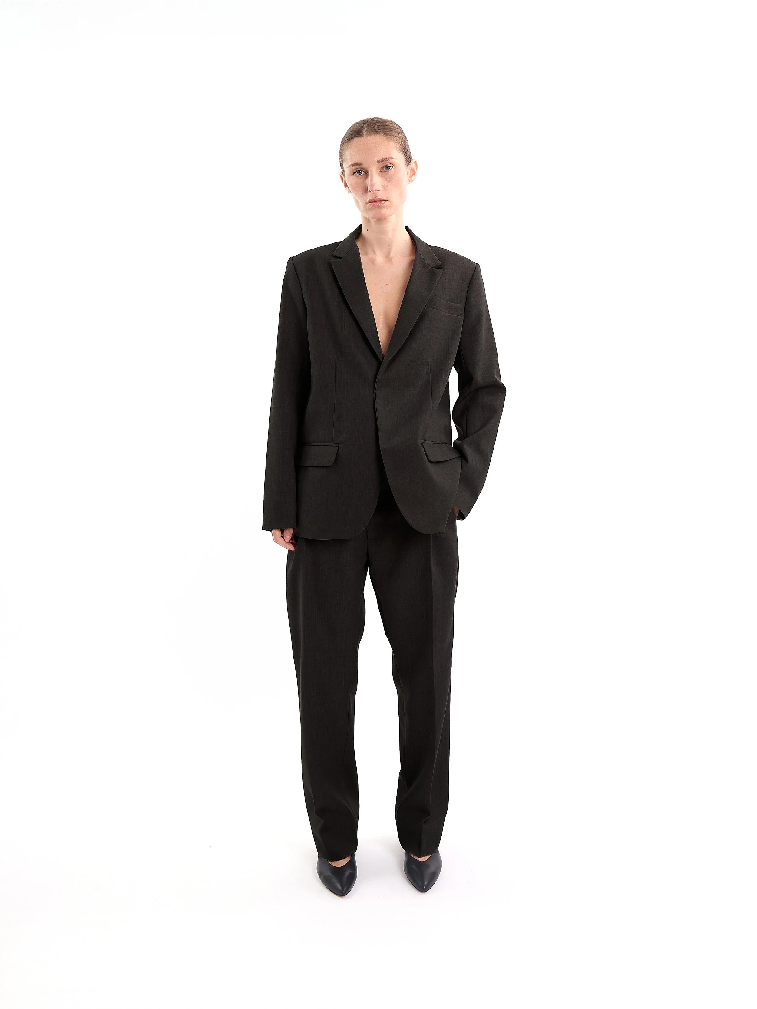 A woman in a black suit standing against a white background. m^