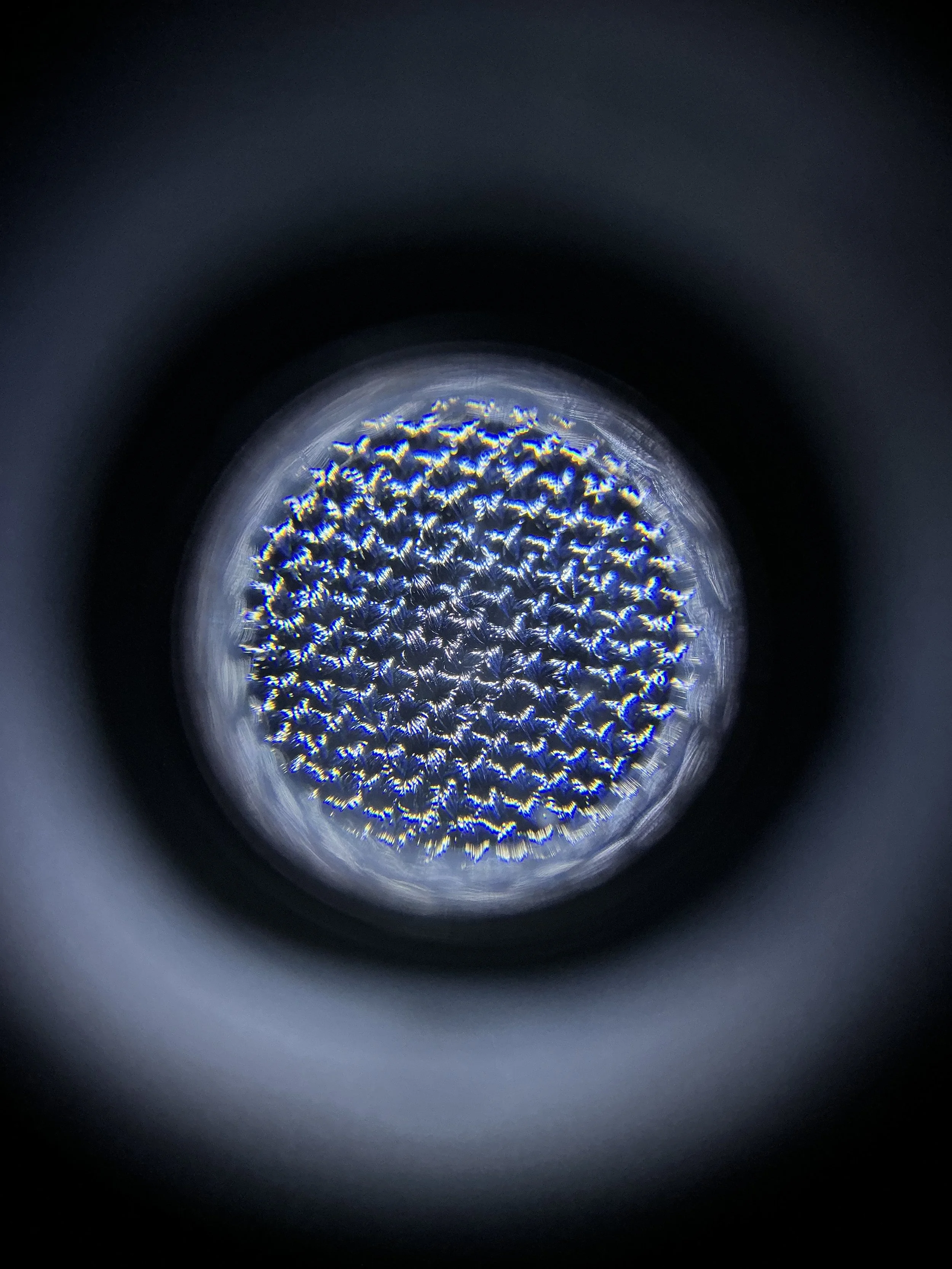 Close-up view inside a metallic object with a textured, honeycomb-like pattern illuminated by blue and white lights, viewed through a circular opening.