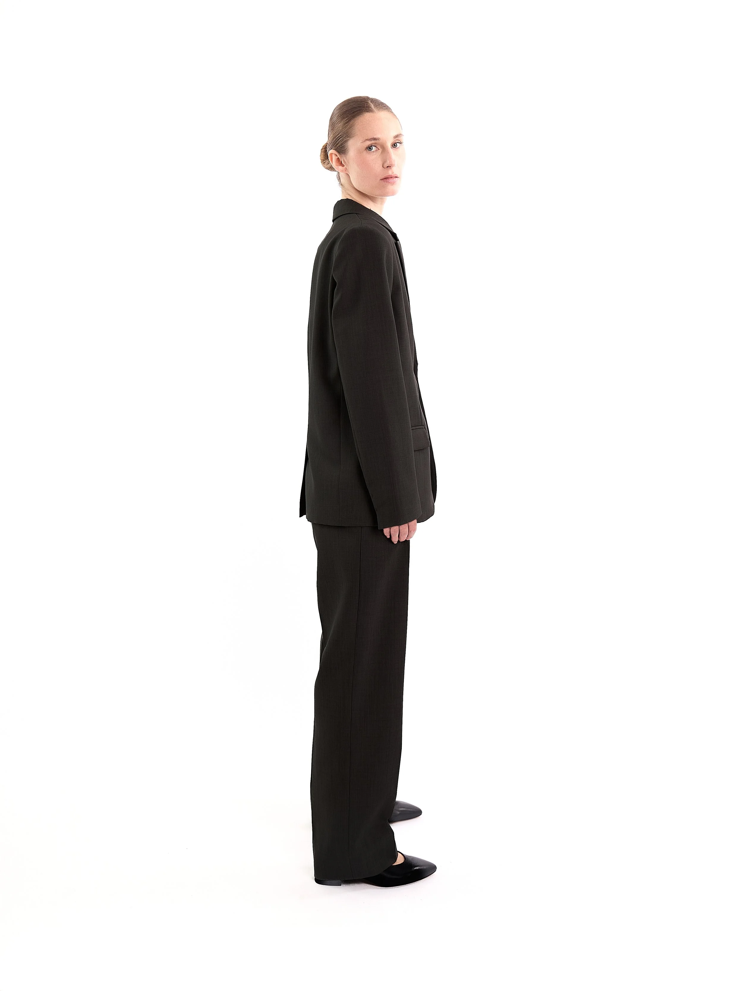 A woman wearing a black suit standing in profile against a white background. m^