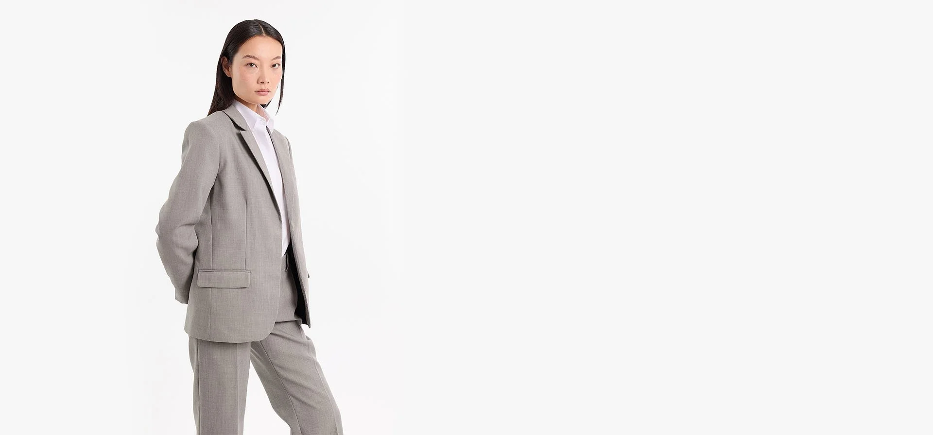 A woman with straight black hair in a business mpower gray suit standing against a plain white background.