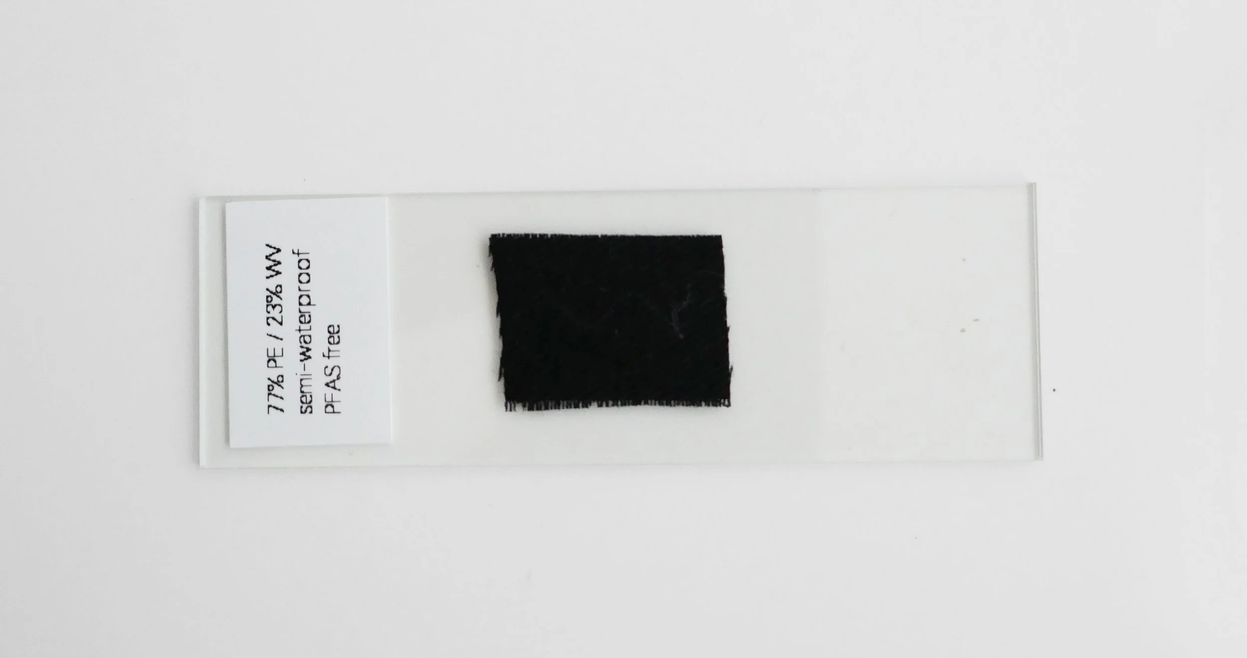 Test strip or sample with a black rectangle on a white background and a small label indicating material composition: 77% PE, 23% W, semi-watertight, PF-AS free.
