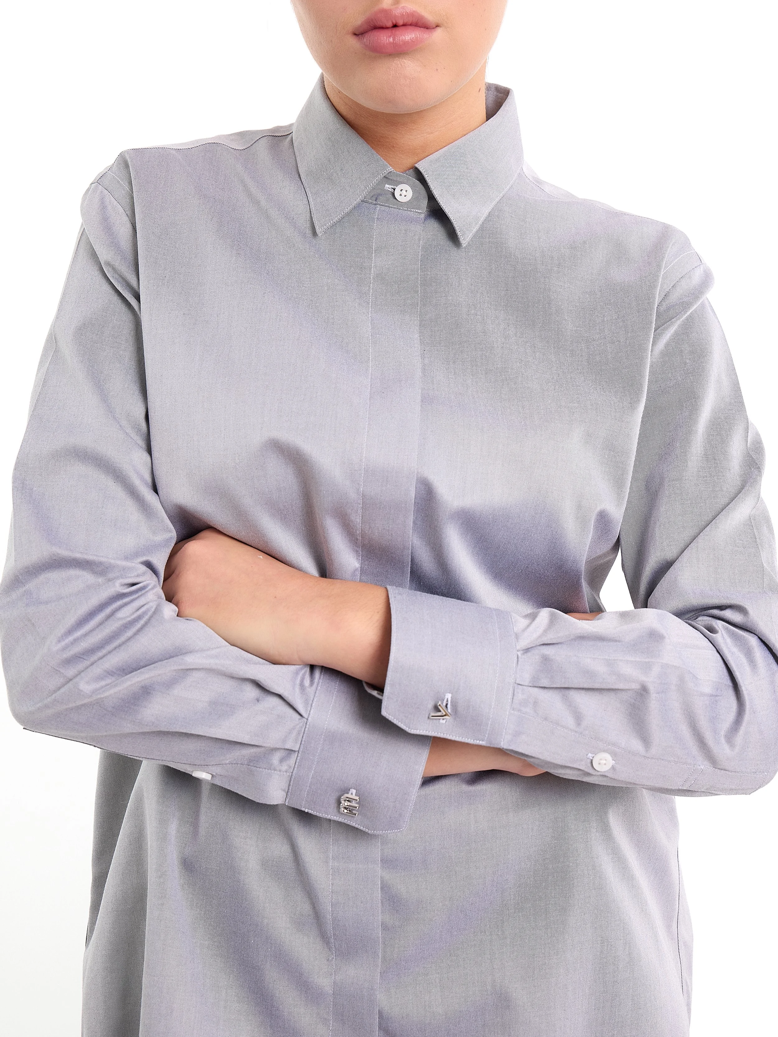 Woman in a light gray button-up shirt with crossed arms. m^