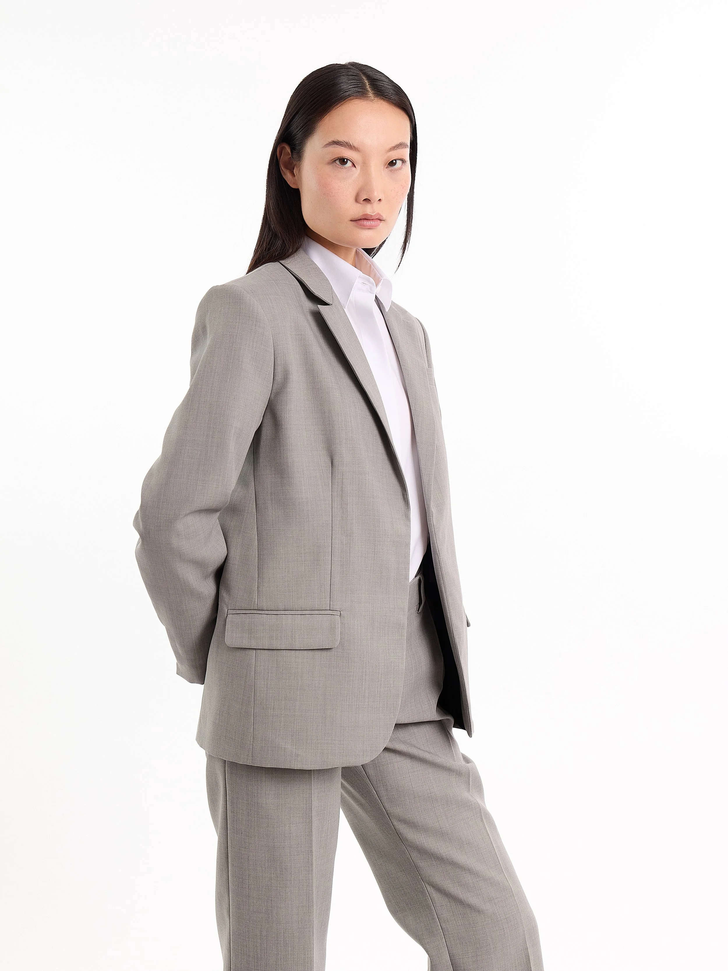 A woman in a gray business suit stands against a white background, looking confidently at the camera. m^