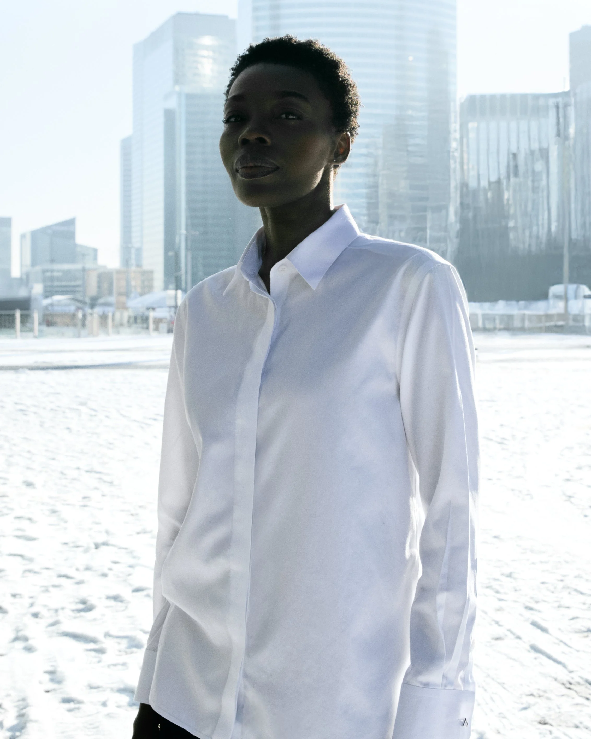 Woman in white shirt standing outdoors in front of modern city buildings during daytime.