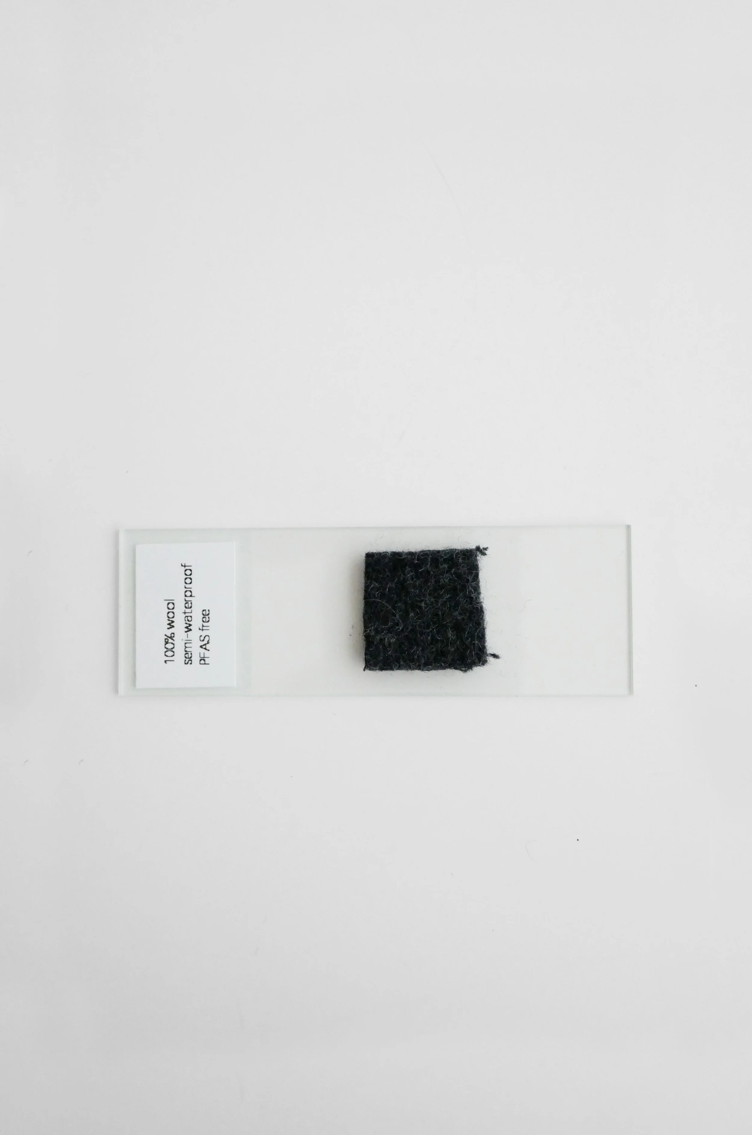 A small square piece of 100% wool felt in black color placed on a transparent background with a label indicating '100% wool, semi-waterproof, PFA's tree'.