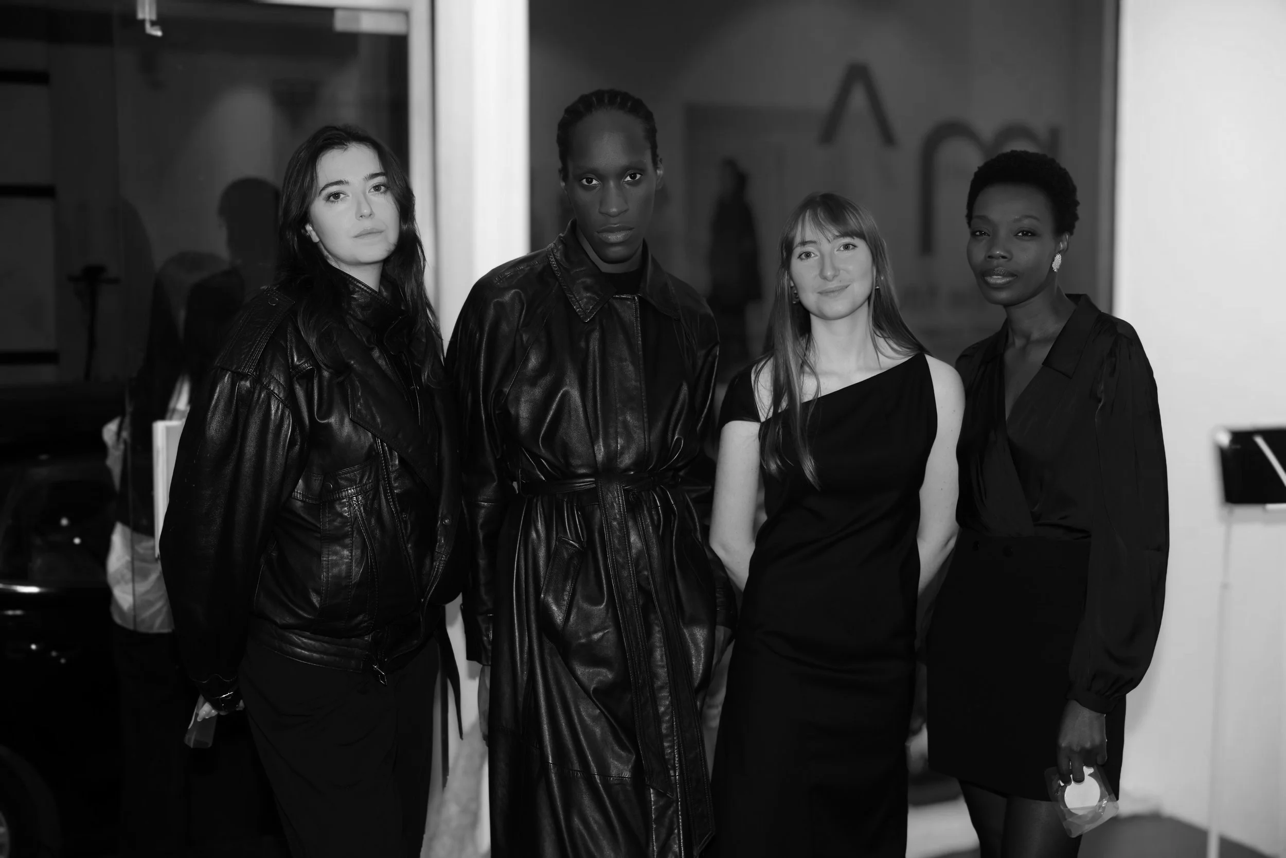 Four women standing together indoors, dressed in black attire, looking at the camera.