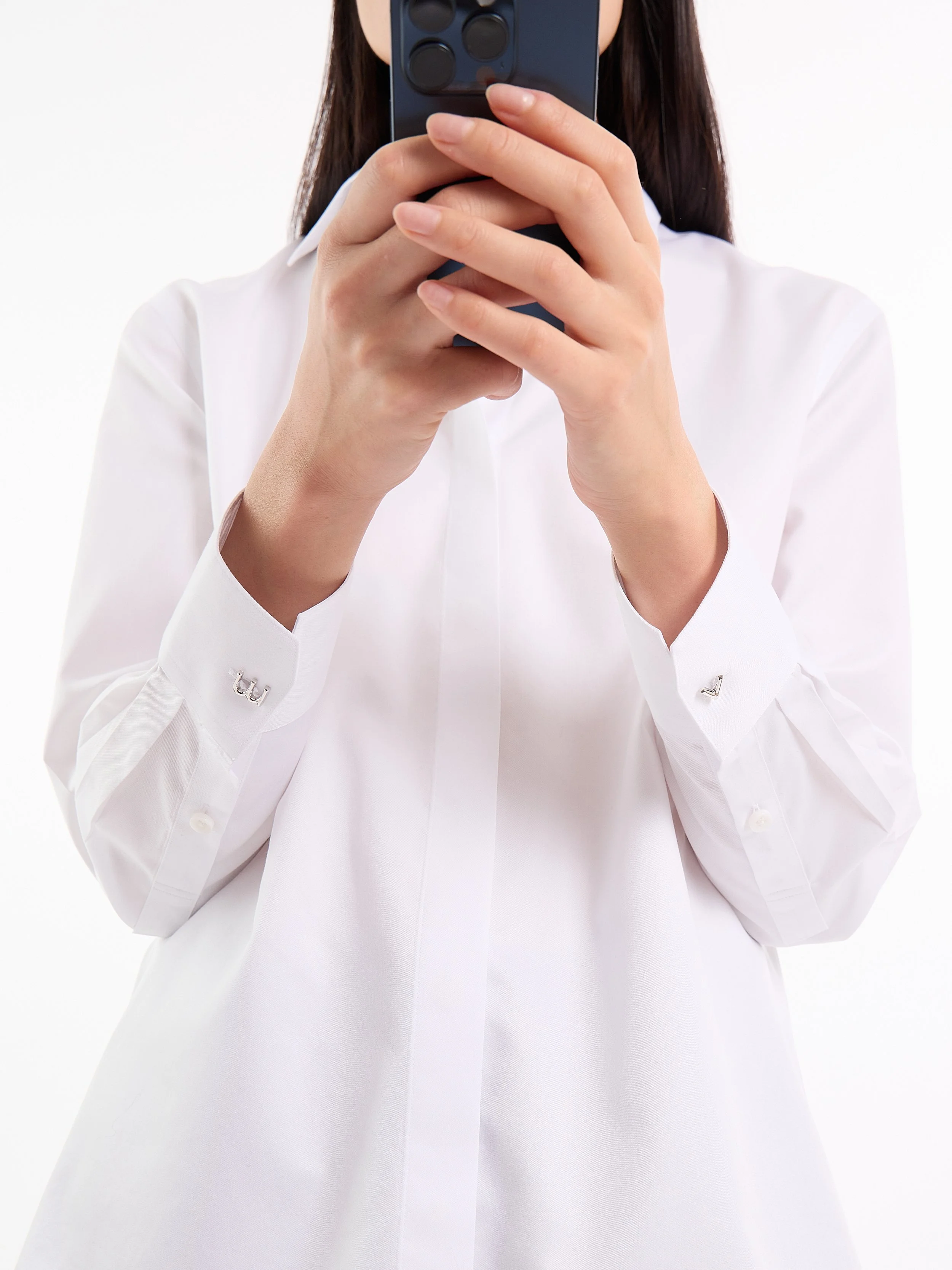 Person in a white shirt holding a smartphone in front of their face. The Classic 0G Shirt is soft, yet structured. Tailored in advanced breathable poplin with non-iron performance. Seam-sealed detailing to bring absolute precision to your day.