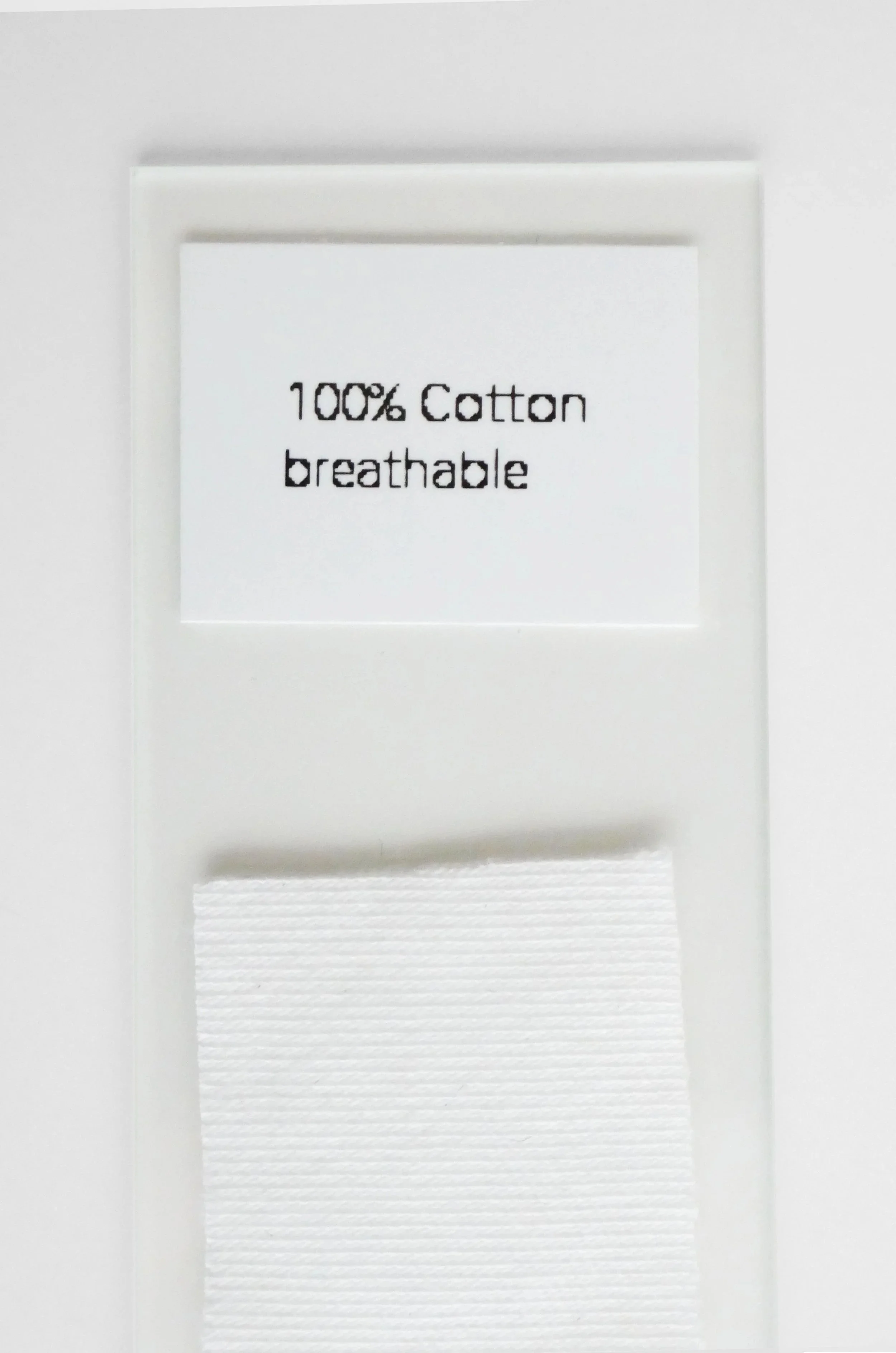 Close-up of a white fabric label with black text indicating it is made of 100% cotton and is breathable.