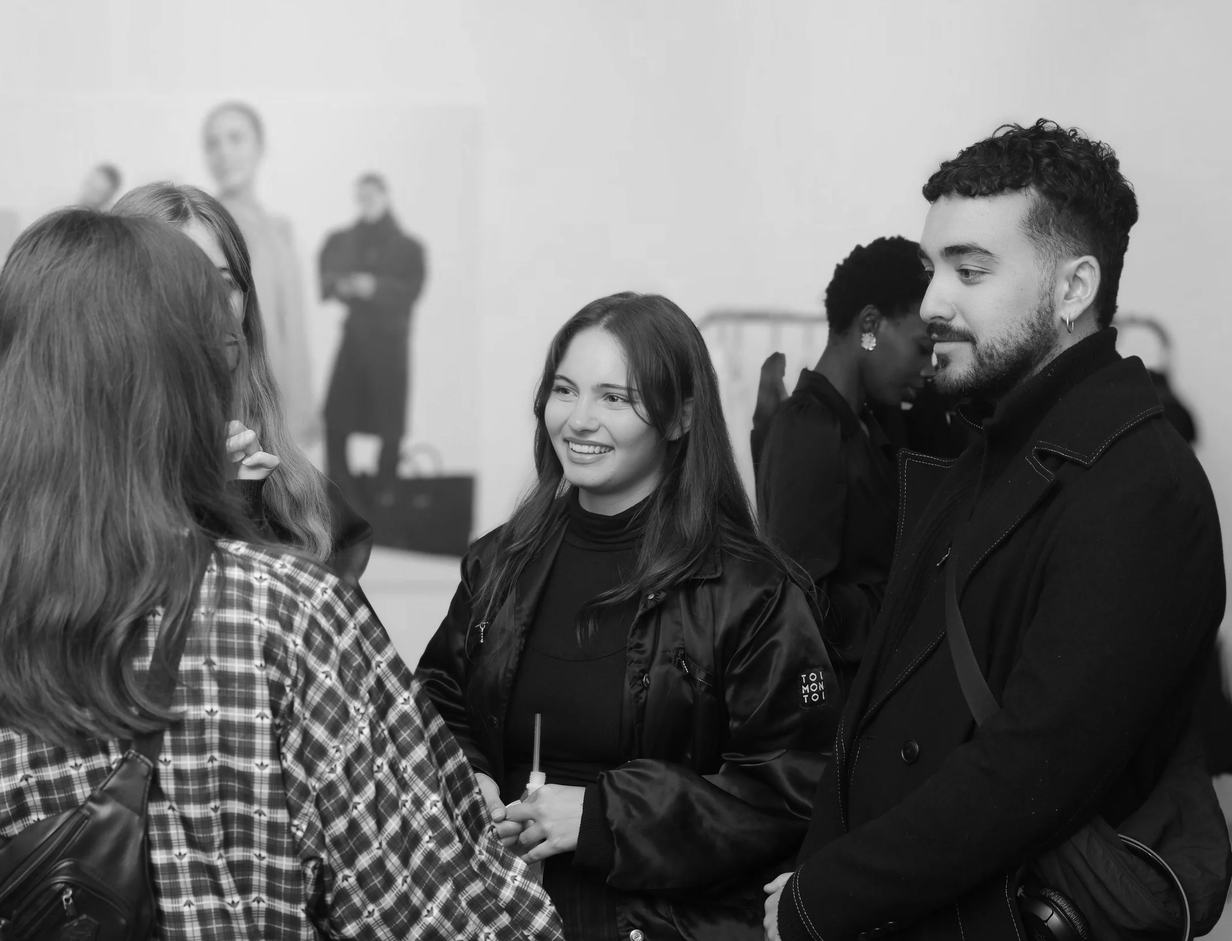 Group of young adults having a conversation at an indoor event, some holding drinks, in black and white.