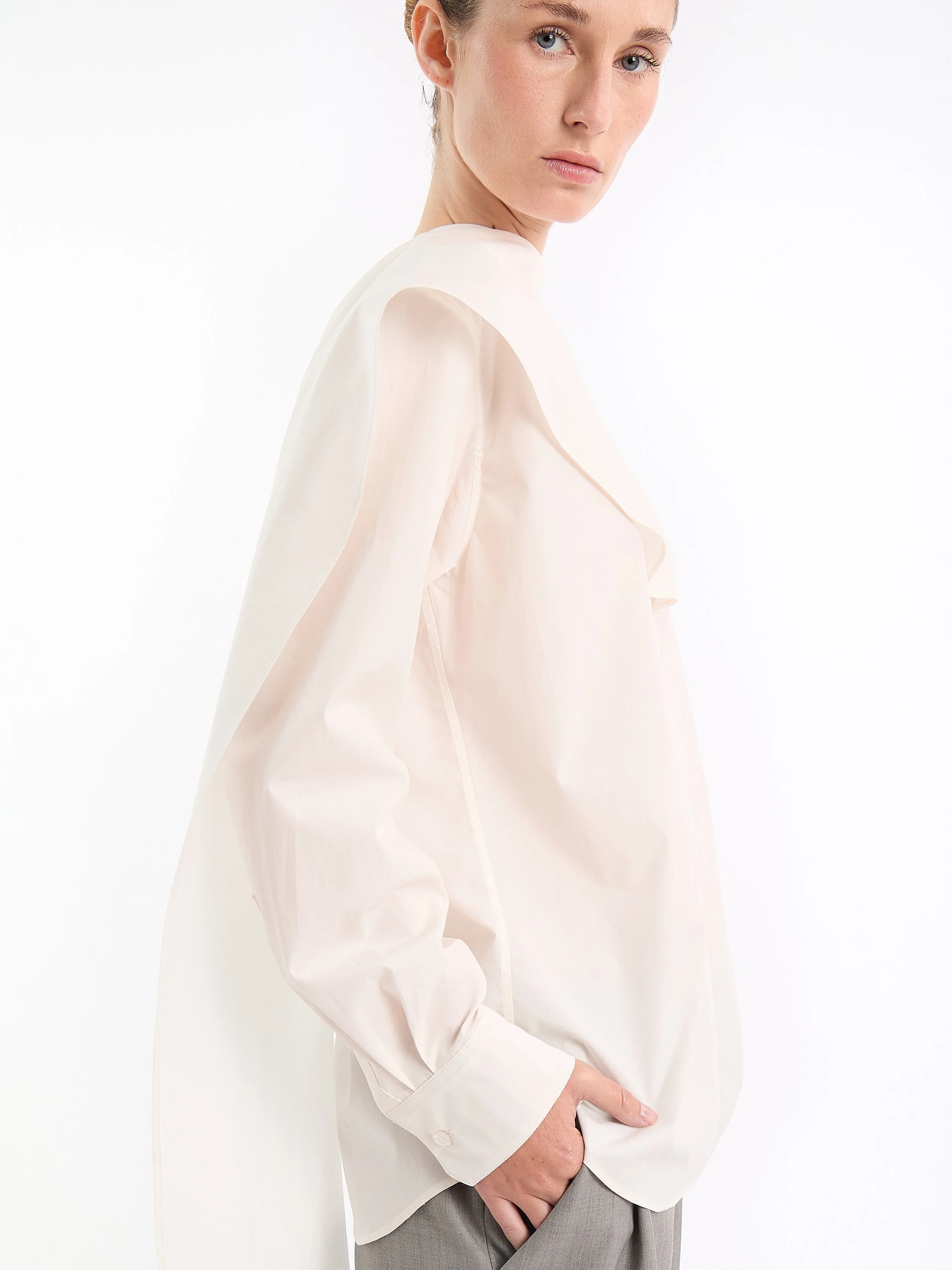 A woman wearing a white blouse with puffed long sleeves and beige high-waisted pants, standing against a plain white background. m^