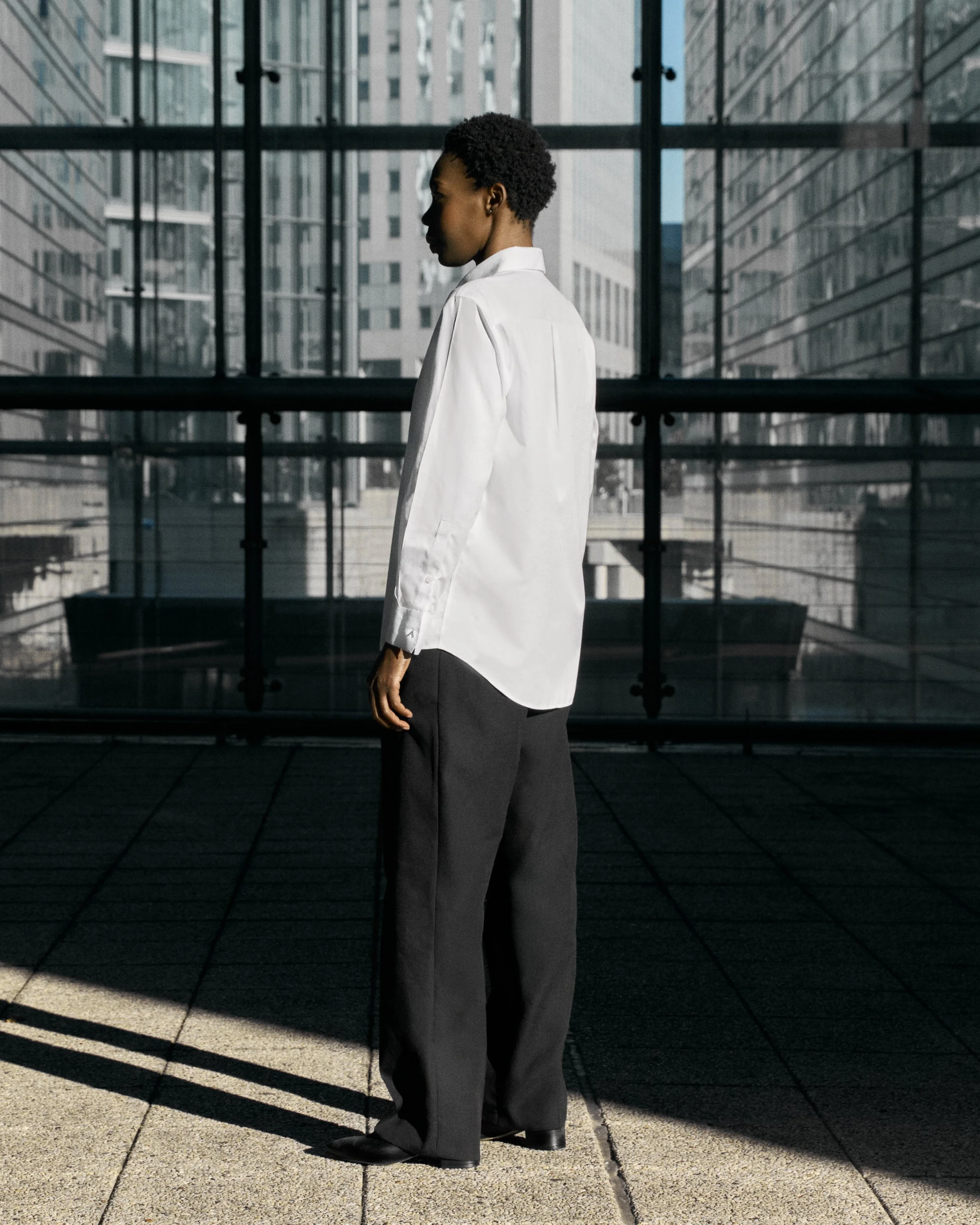 Woman in white shirt and black pants standing in a modern glass building with city view.