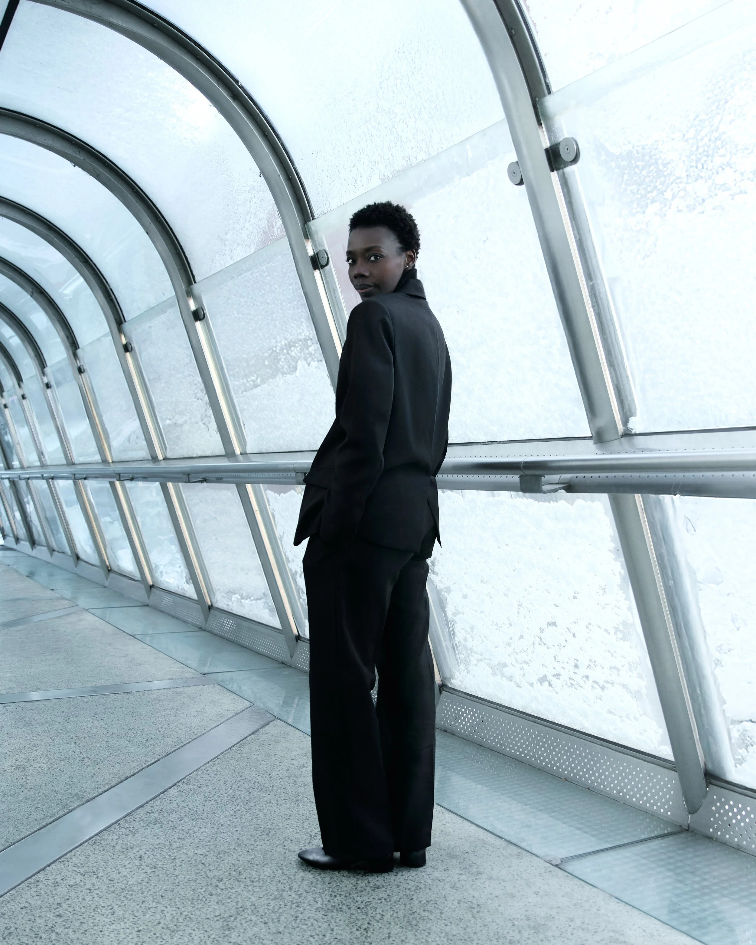 A woman dressed in a black suit standing in a glass tunnel with snow outside.