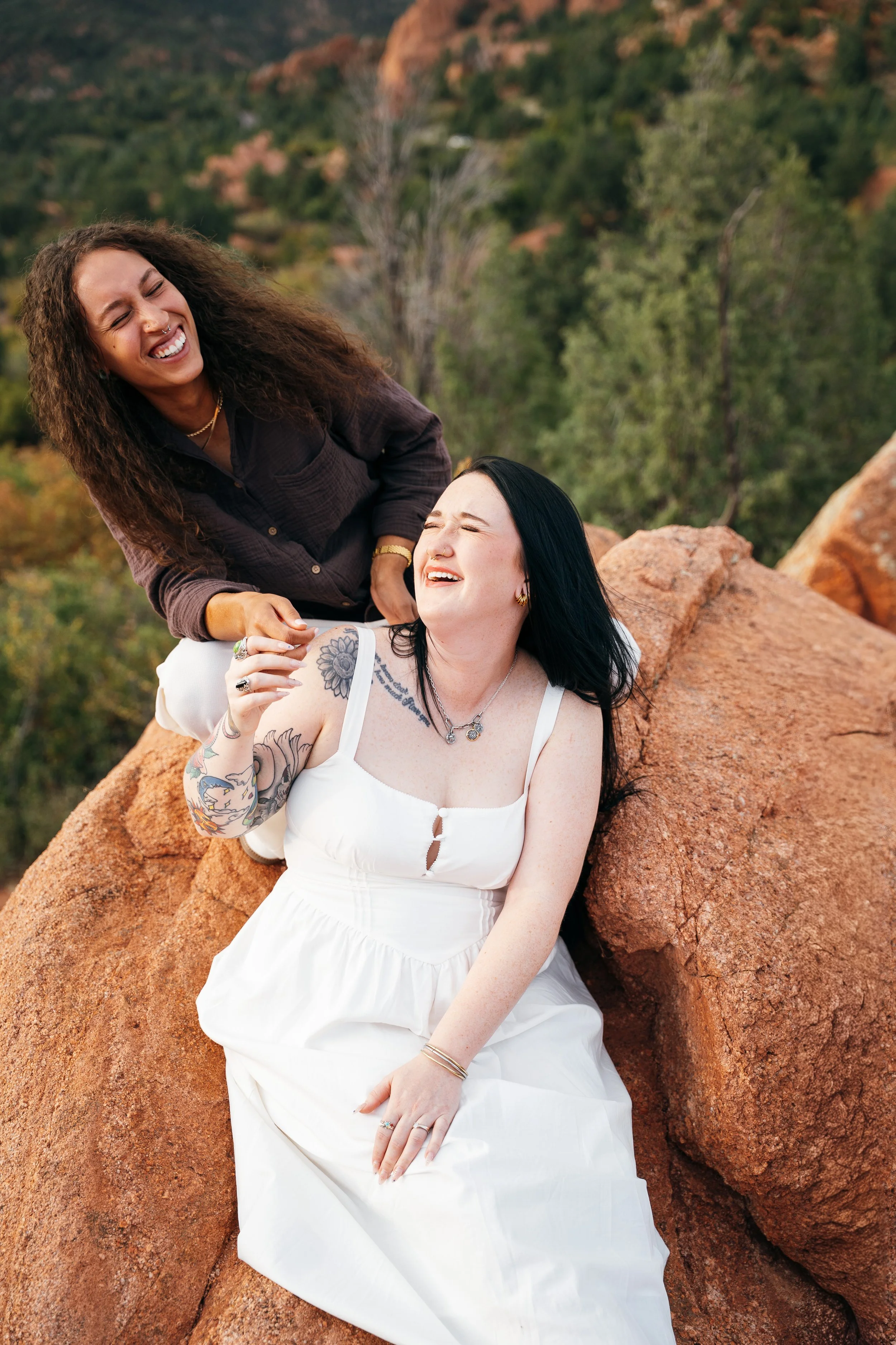  Amber and Kelsey laughing together while sitting on a red sandstone rock formation. 