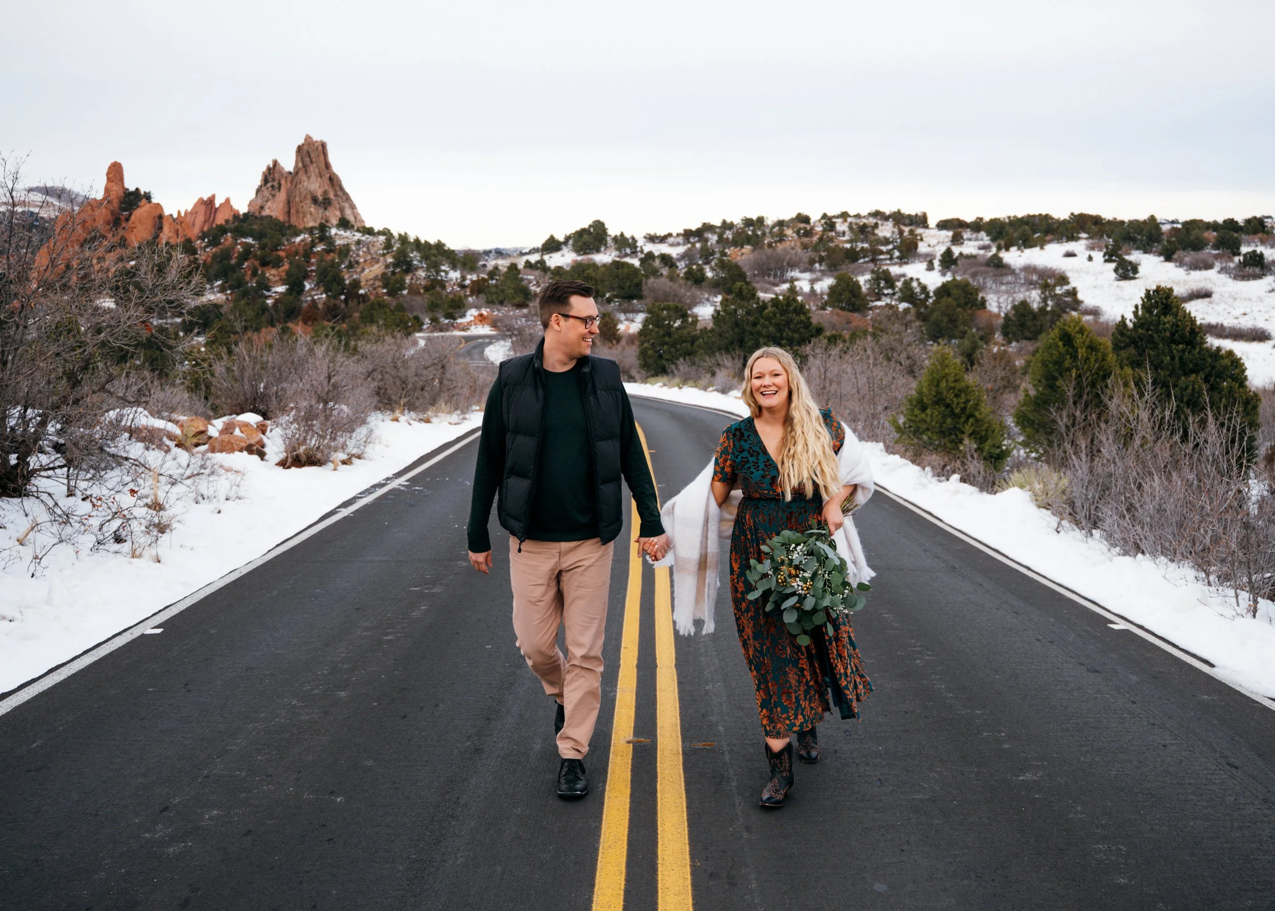 Expectant couple walking together on a snowy road during a January maternity session near Garden of the Gods in Colorado Springs