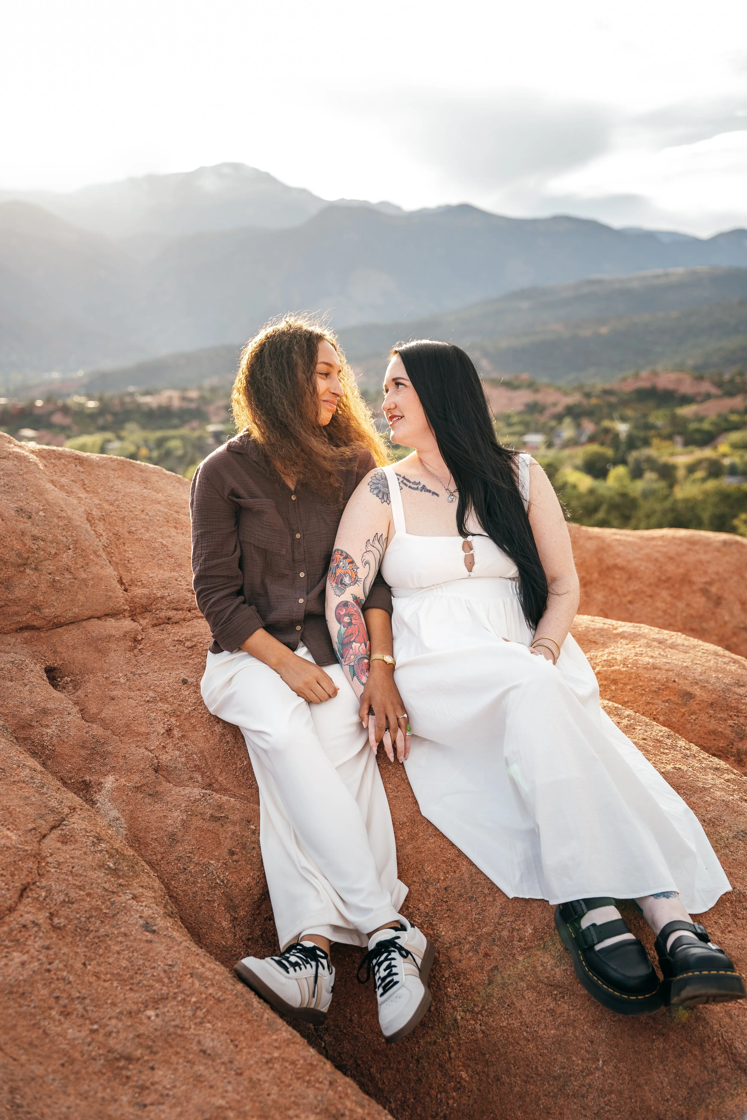 Amber and Kelsey sitting together on red sandstone with distant mountains behind them.