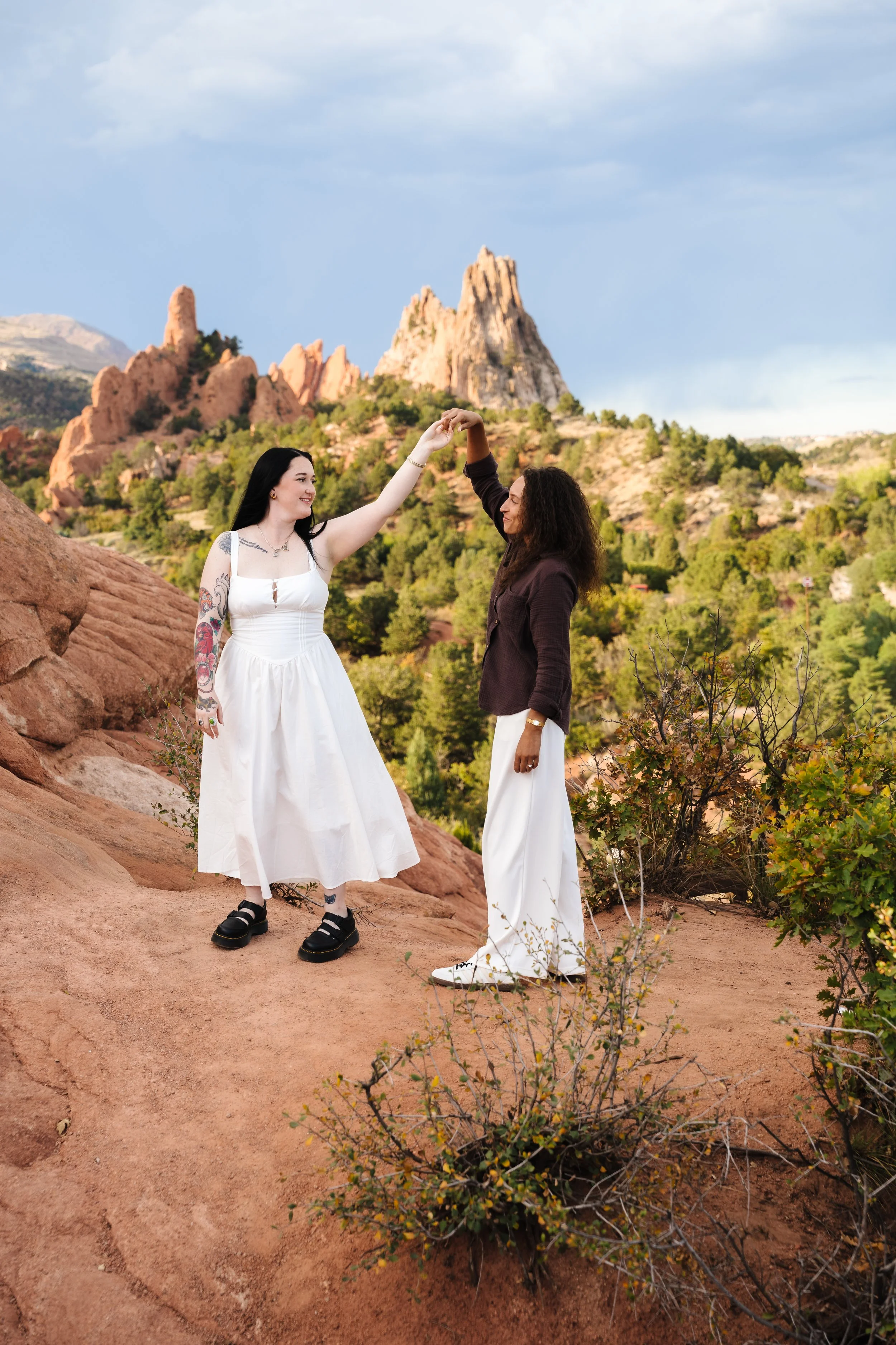 Amber and Kelsey sharing a playful twirl with towering red sandstone formations behind them at Garden of the Gods