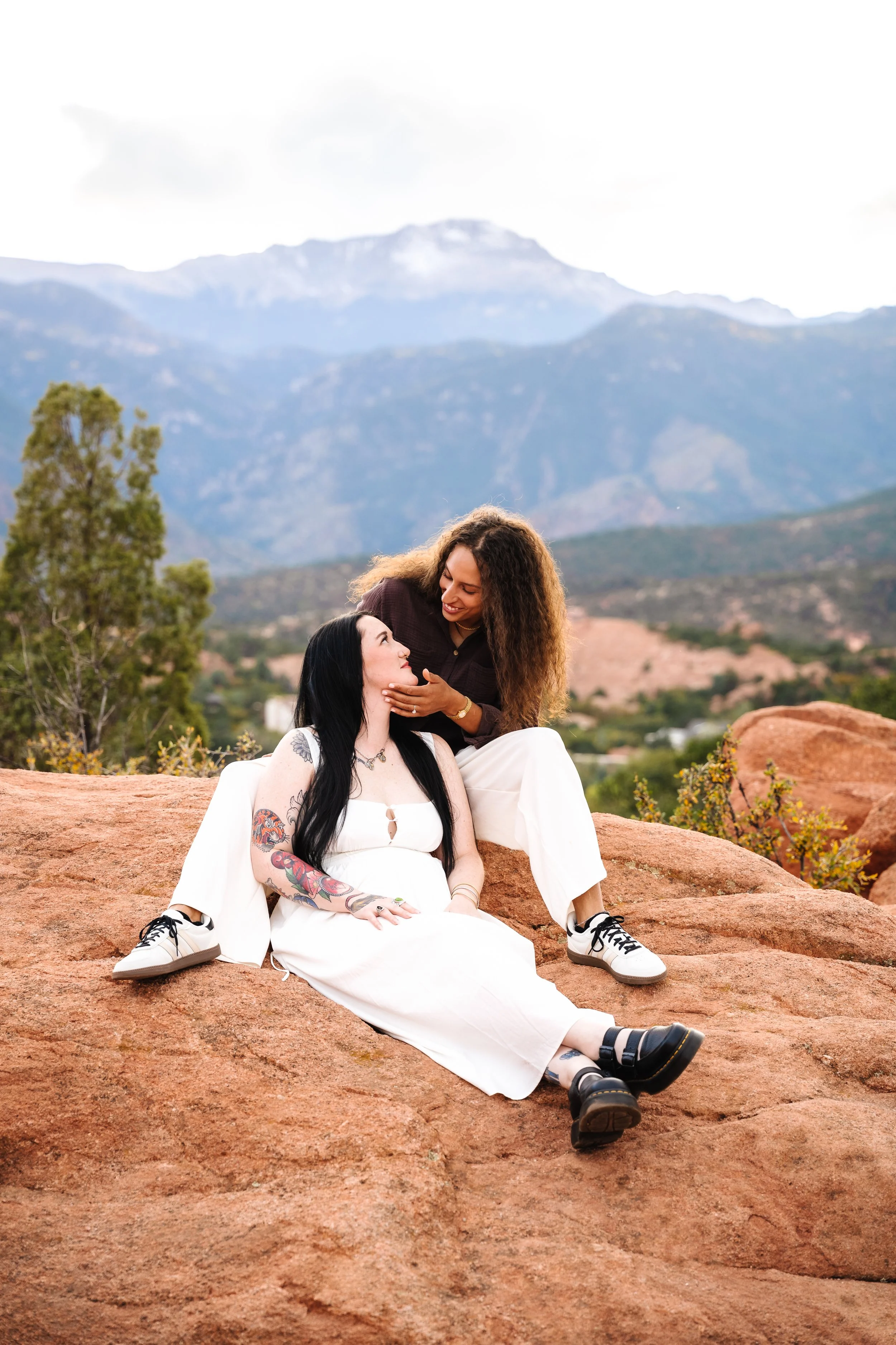 Amber and Kelsey seated on red rocks with Pikes Peak and the surrounding Colorado mountains in the background