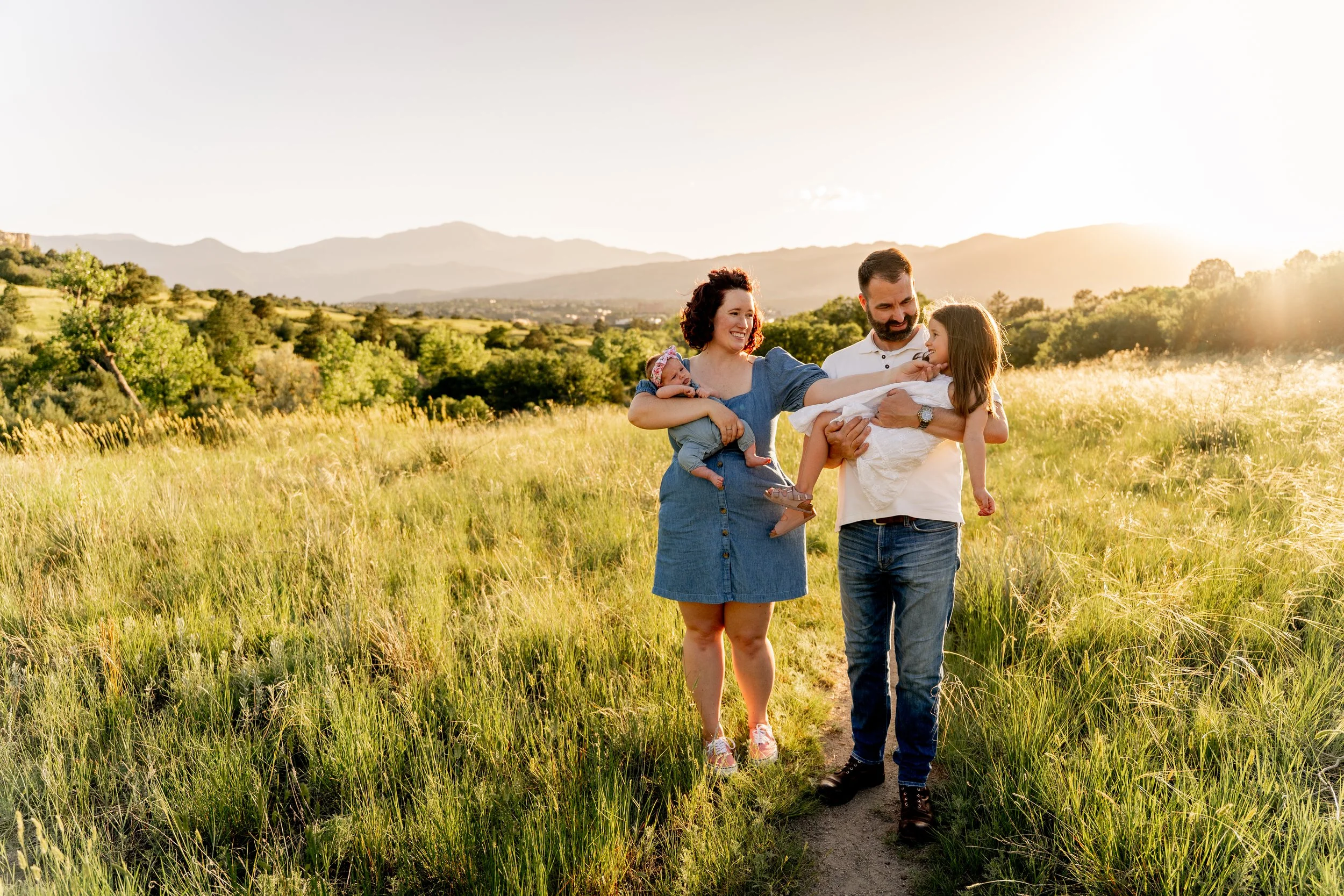 Family of four enjoying a relaxed outdoor photography session in a sunlit Colorado Springs meadow during golden hour. Natural, candid family photography focused on genuine connection and joyful moments by Colorado Springs family photographer Sarah K.