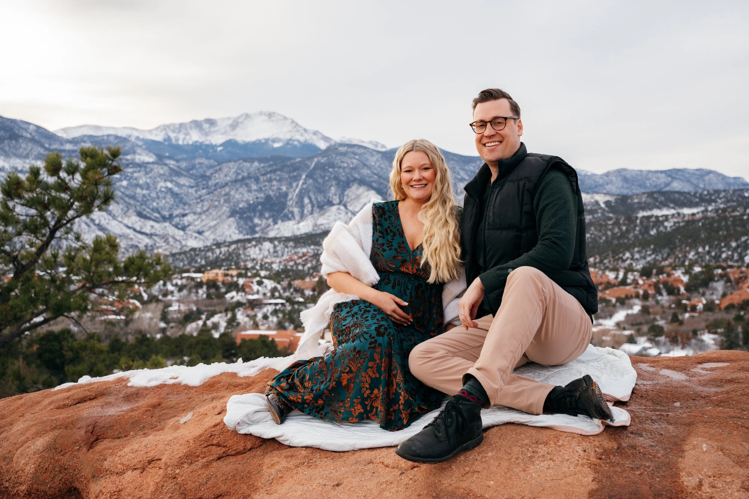 Couple sitting together on red rocks during a snowy winter maternity session in Colorado Springs