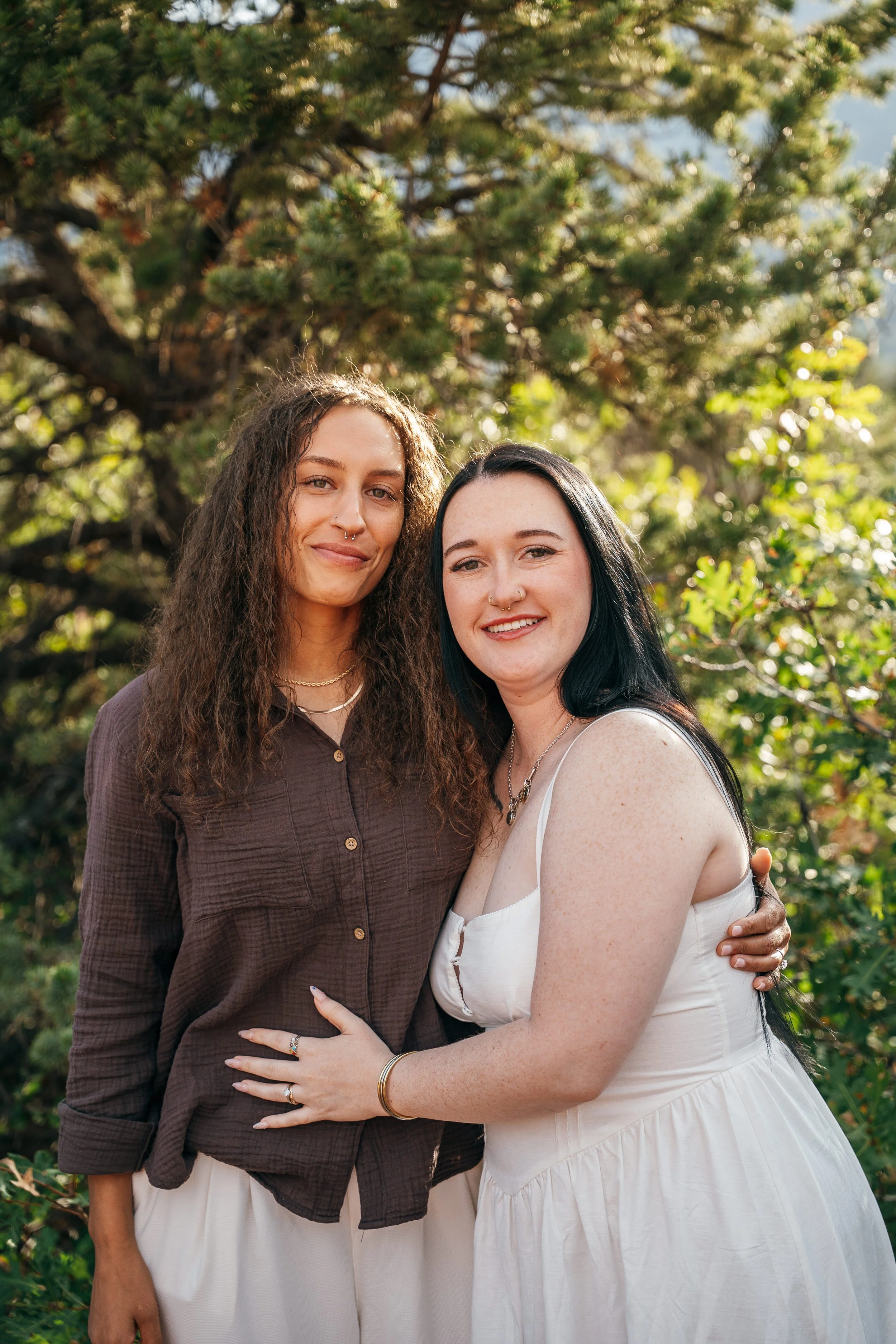 Two women standing close together for a portrait surrounded by pine trees at Garden of the Gods.