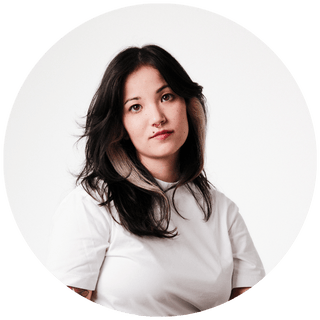 Porträt einer jungen Frau mit dunklen, gewellten Haaren, weißem Hemd, vor weißem Hintergrund.