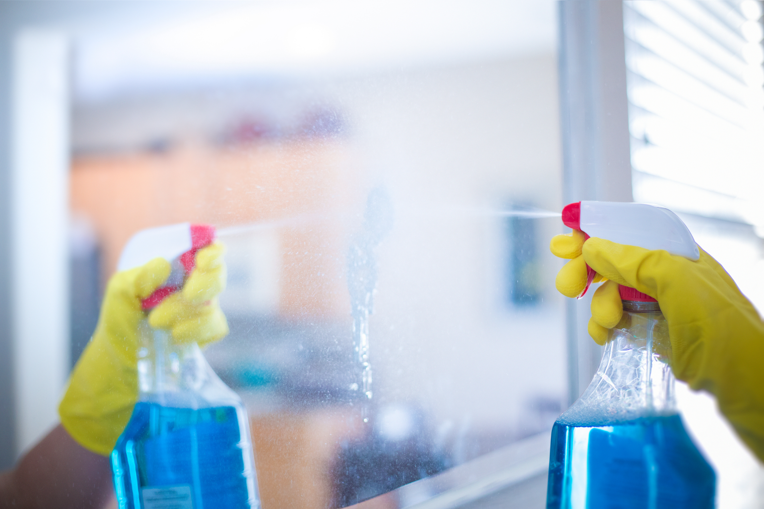 Person wearing yellow gloves using spray bottles to clean a glass window.