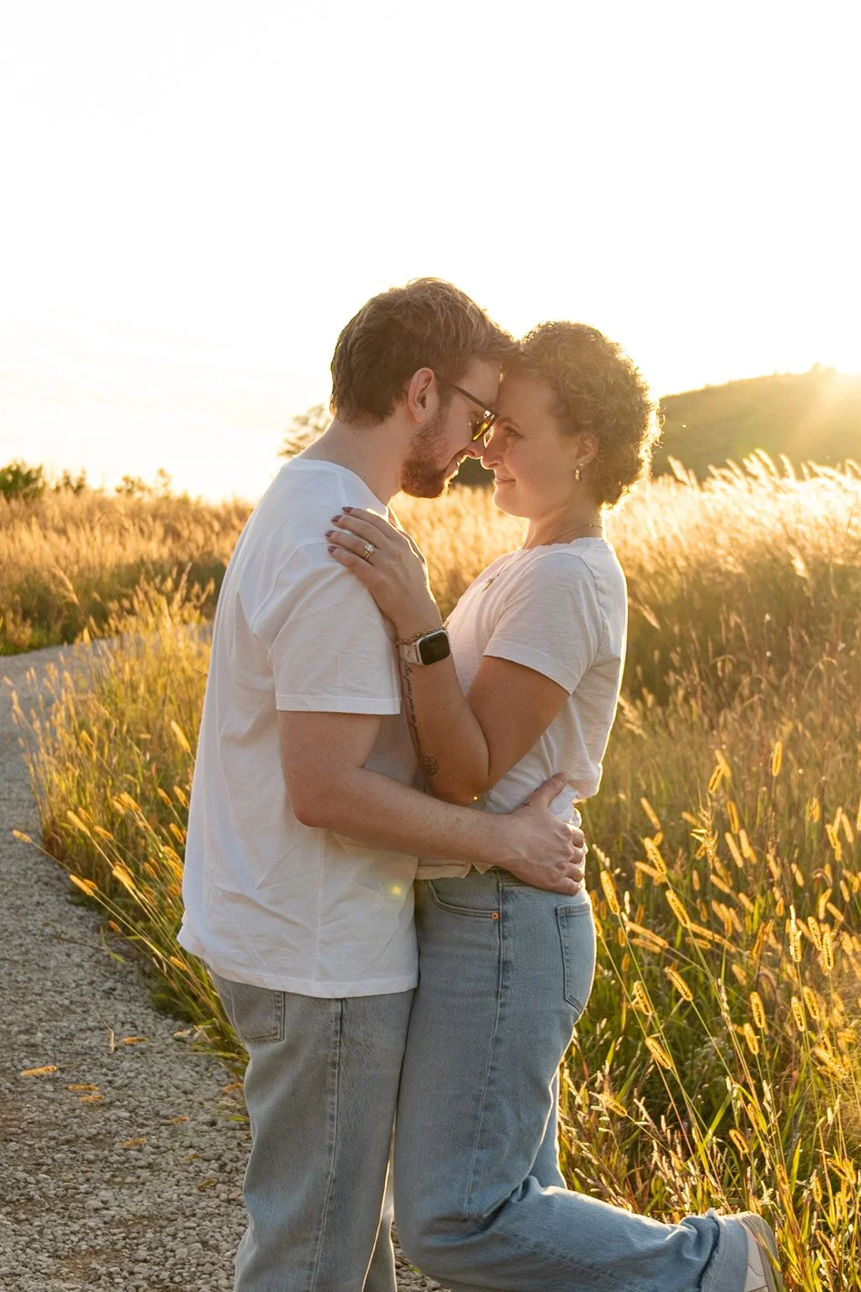 A couple embracing and touching foreheads in a field of tall grass during sunset.