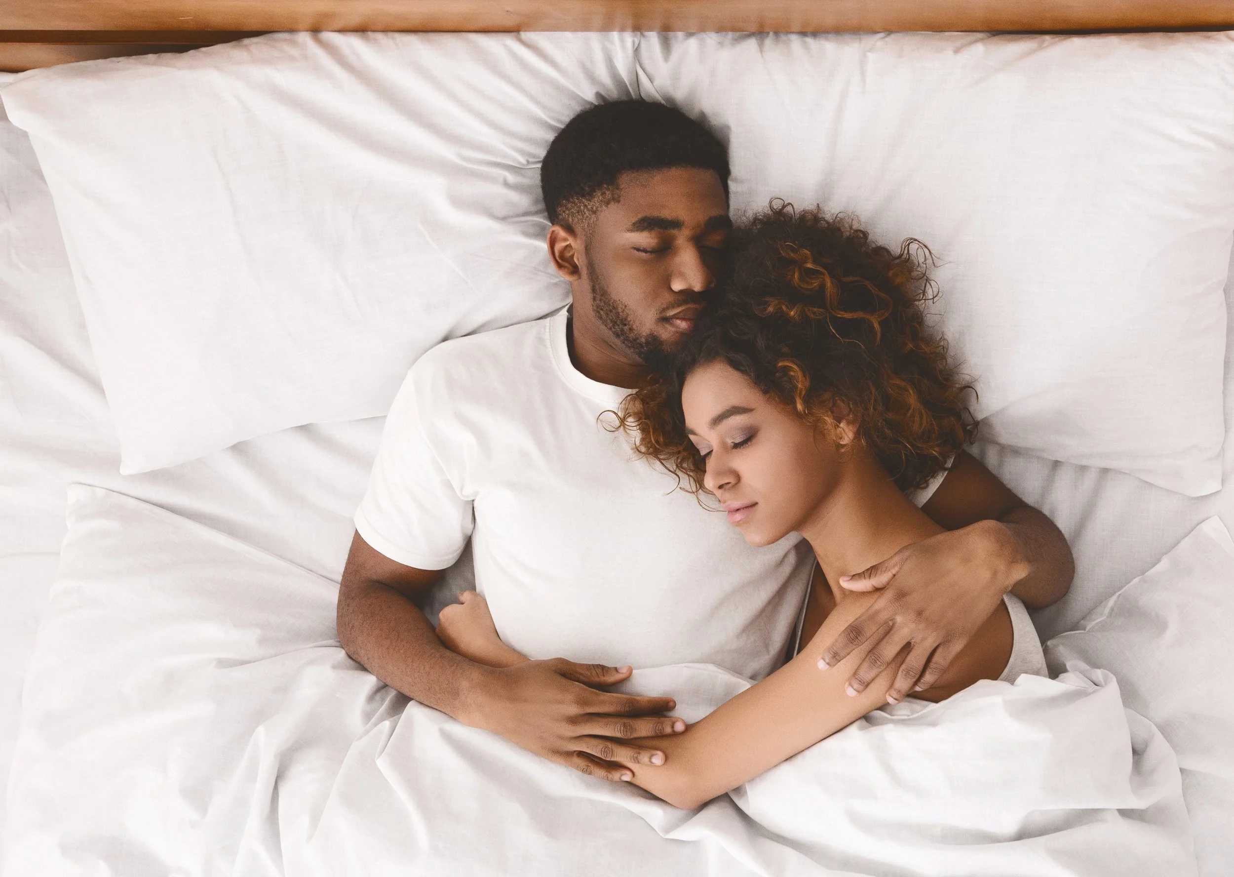 A young couple sleeping together in a bed, cuddling peacefully.