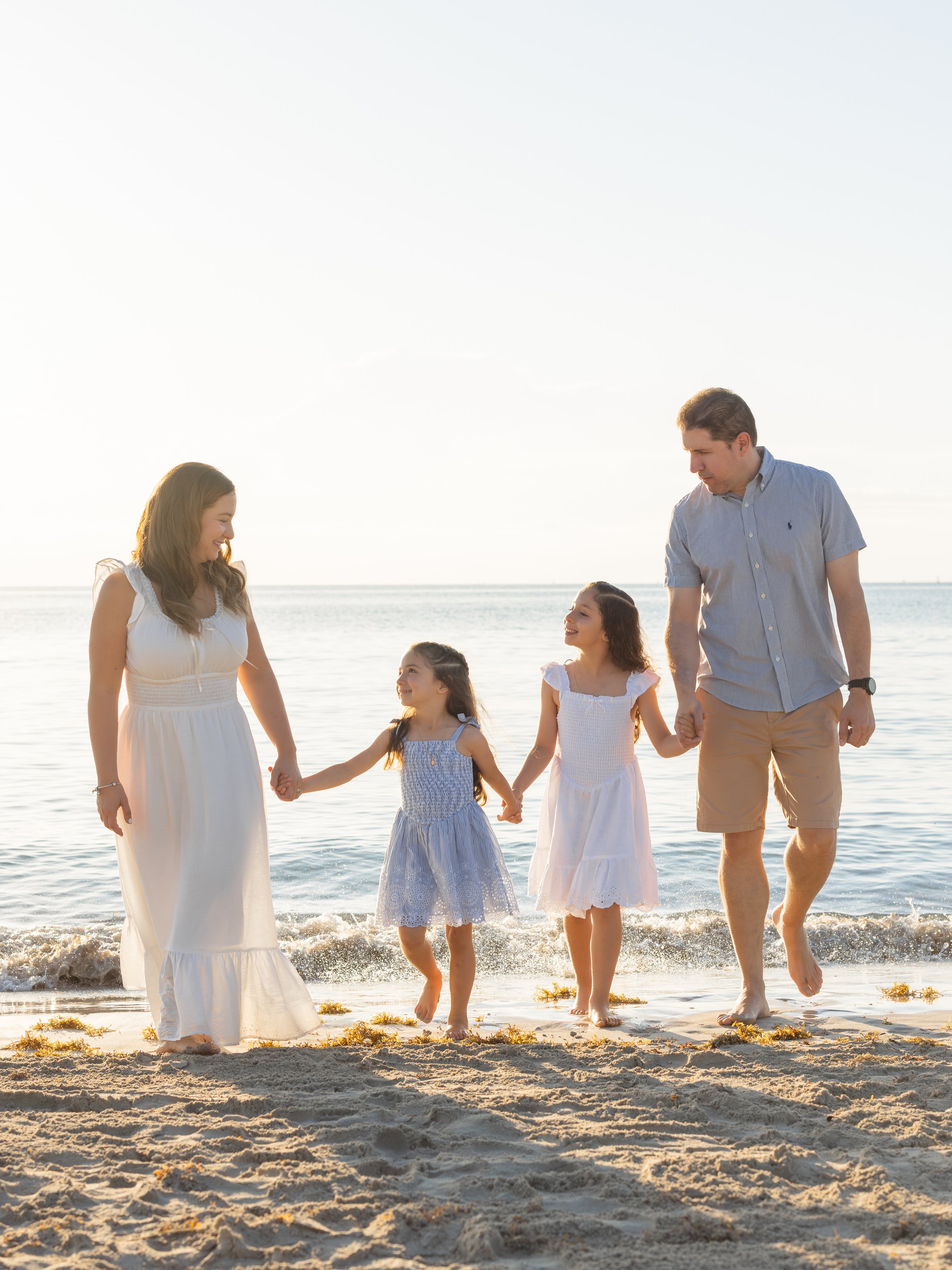A family of five walking hand in hand along the beach at sunset, smiling and enjoying each other's company.