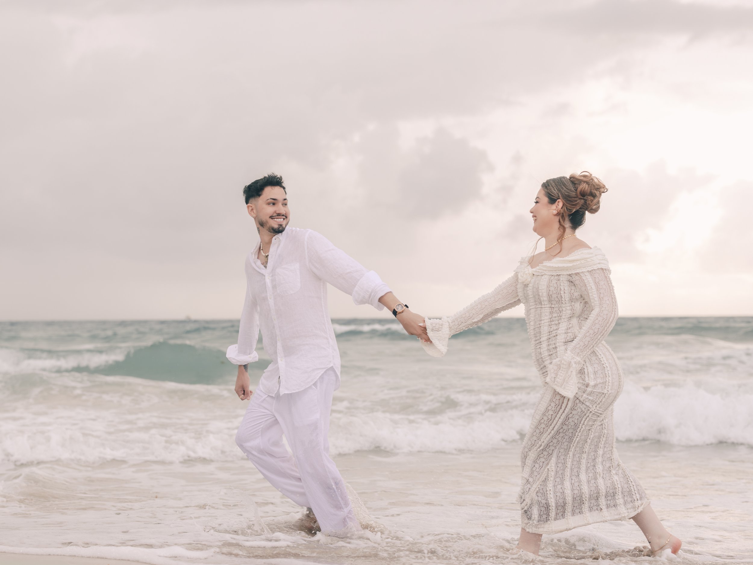 A couple holding hands and walking along the beach during a cloudy day.