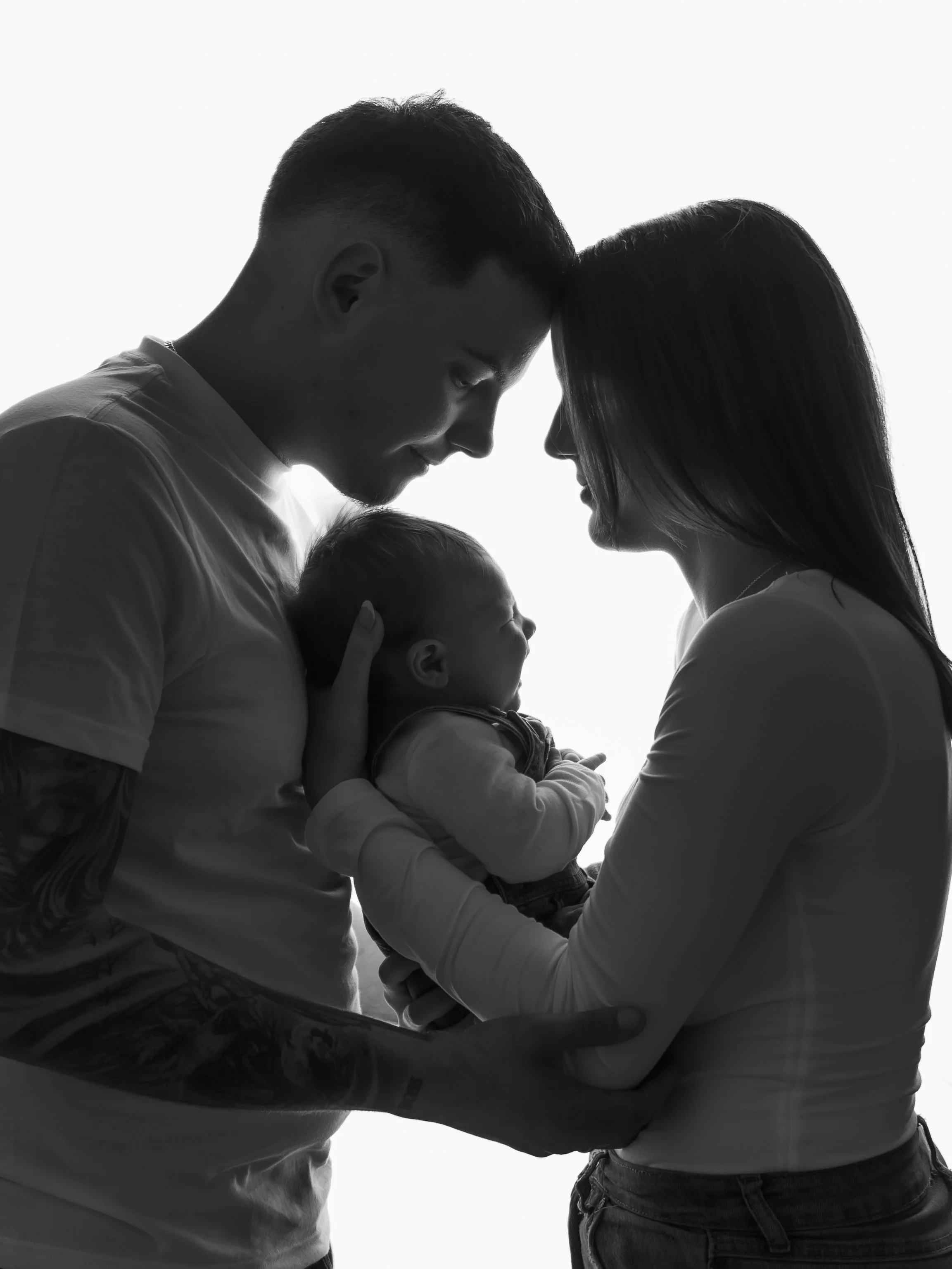 Silhouette of a man and woman holding a newborn baby close to each other, with their foreheads touching.