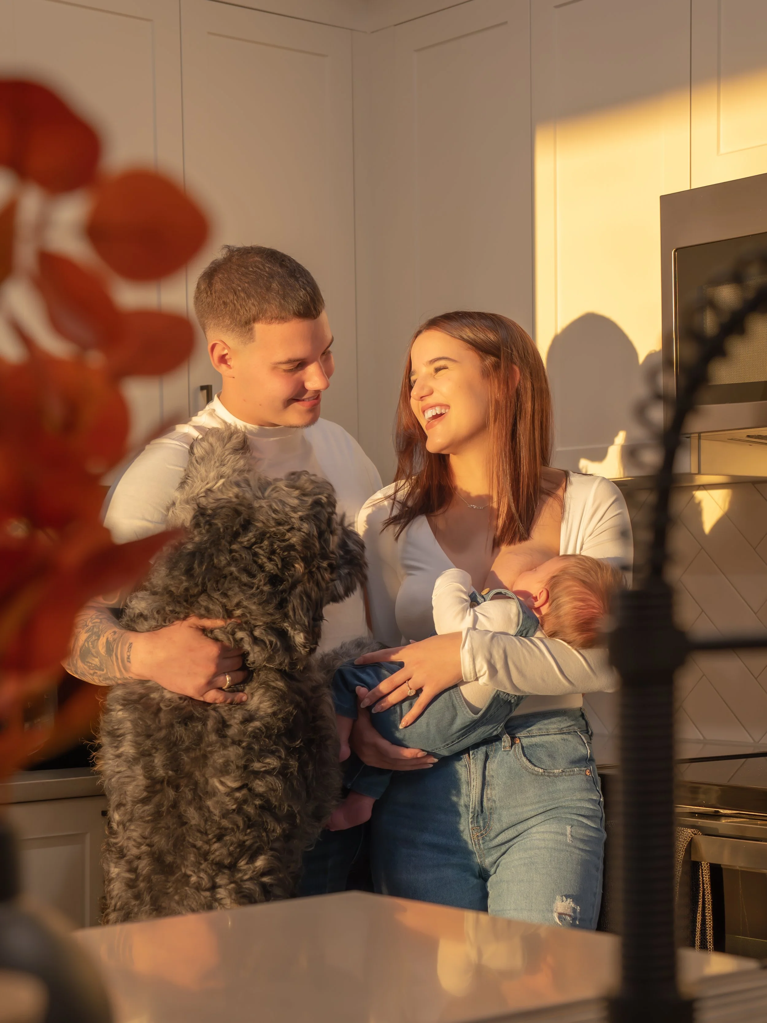 A smiling family of four, including a man, a woman, a young girl, and a large dog, enjoying a moment together in a kitchen with warm sunlight in their central florida apartment.