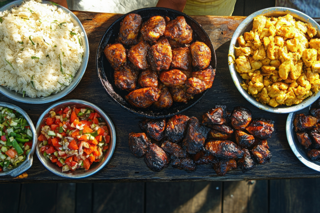 Assorted plates of Nigerian food including jollof rice, fried chicken, fried fish, scrambled eggs, and vegetable salads on a wooden table.