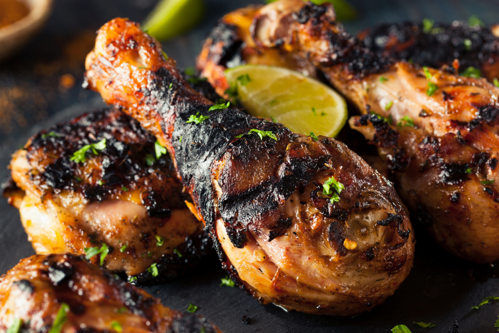 Close-up of grilled chicken drumsticks garnished with chopped herbs and lime wedges.