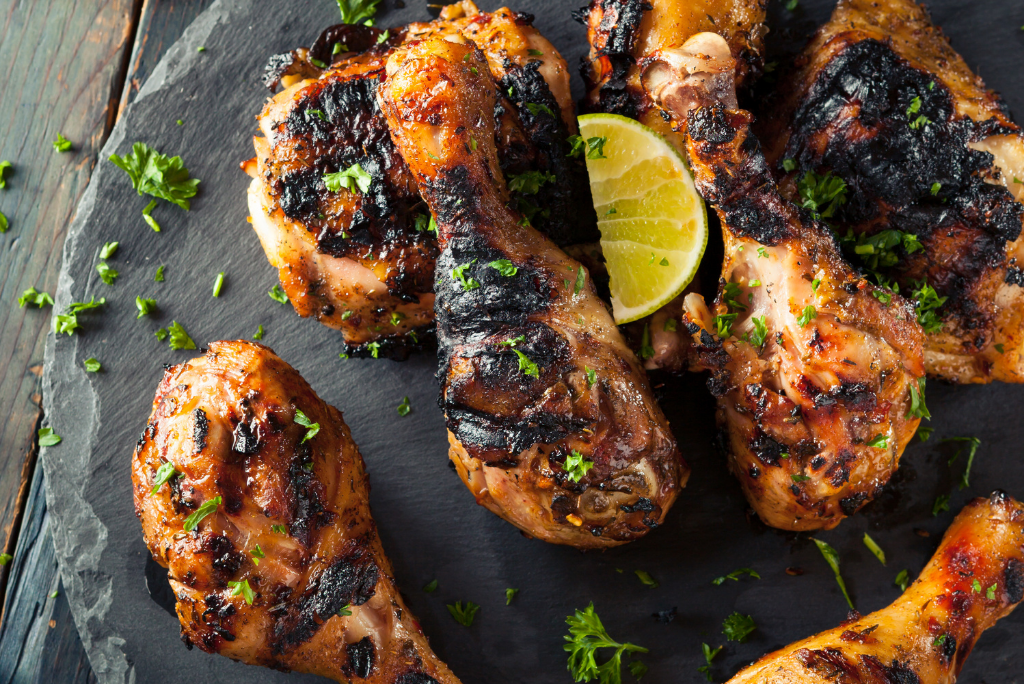 Grilled chicken drumsticks garnished with chopped herbs and a lime wedge, placed on a dark slate platter.