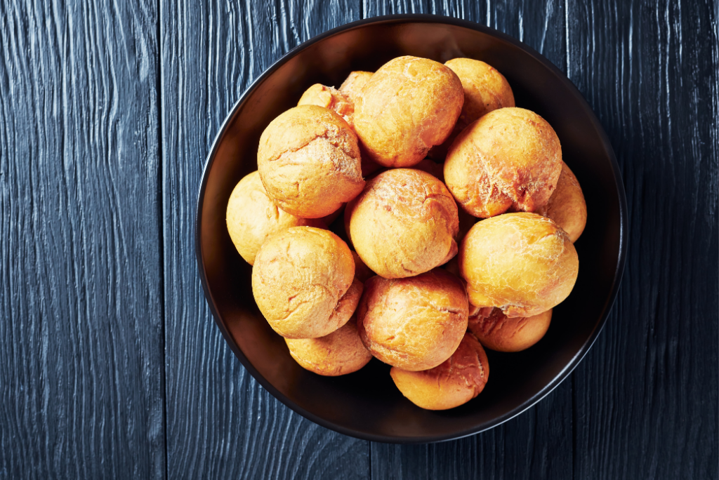 A black bowl filled with small, round, golden-brown bread rolls on a dark wooden surface.
