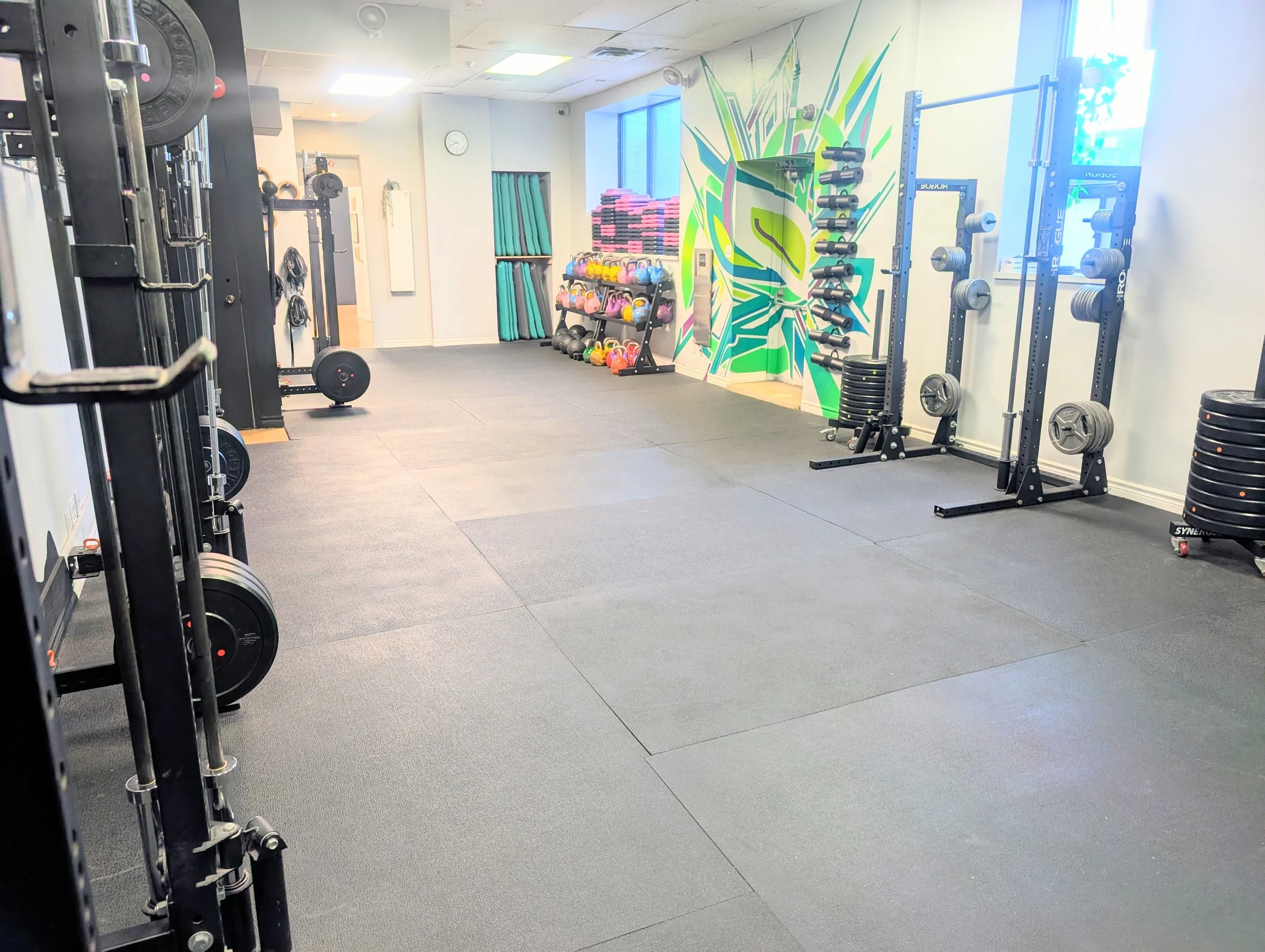 Empty gym with various equipment including weight racks, kettlebells, and a painted wall mural.