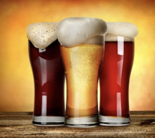 Three glasses of beer, each with a foamy head, placed on a wooden surface with a warm yellow background.