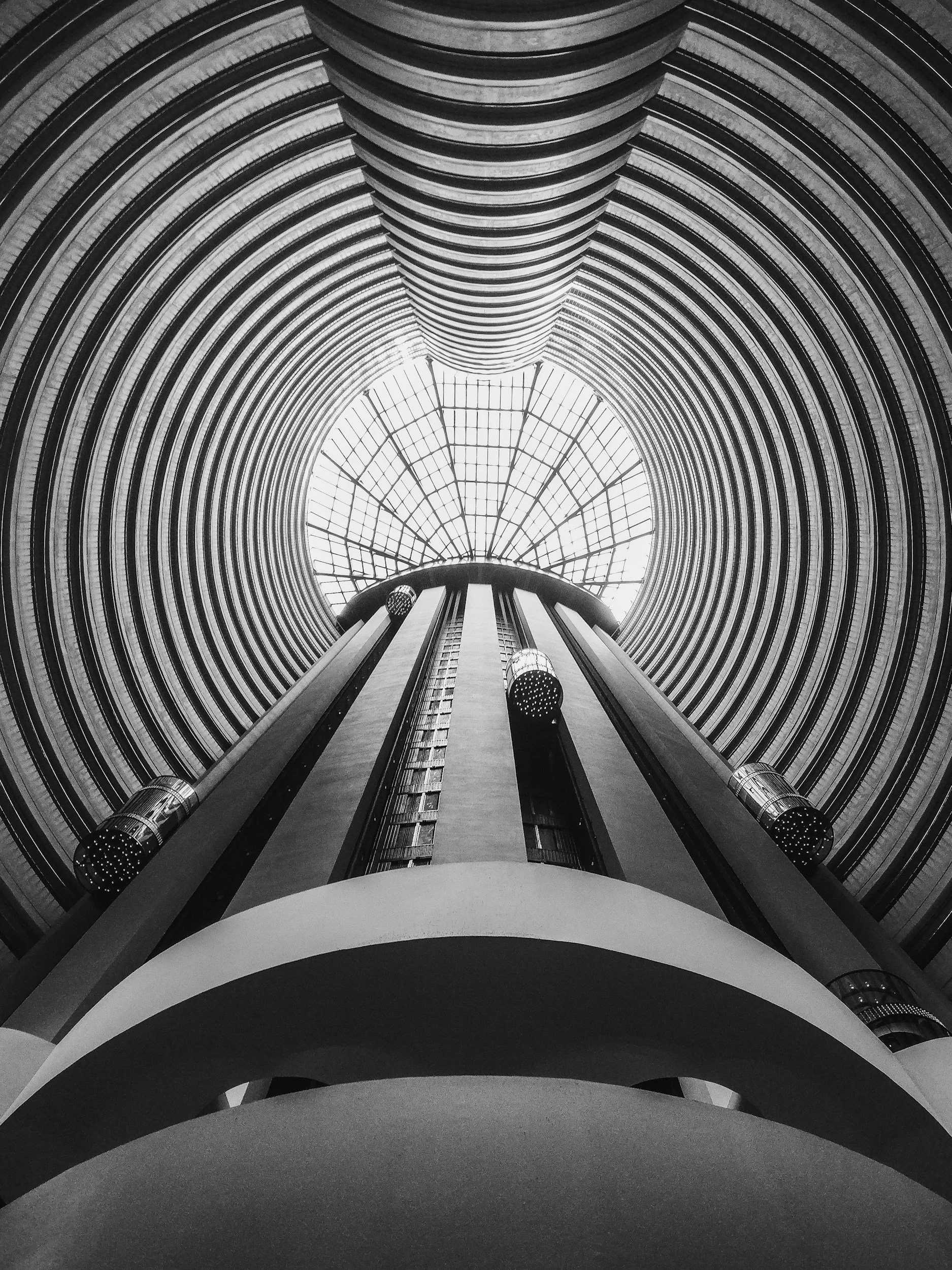 Two men sitting close together in front of a laptop, viewing a screen with emails or messages, one wearing glasses and the other wearing a cap, in a dimly lit office or workspace.