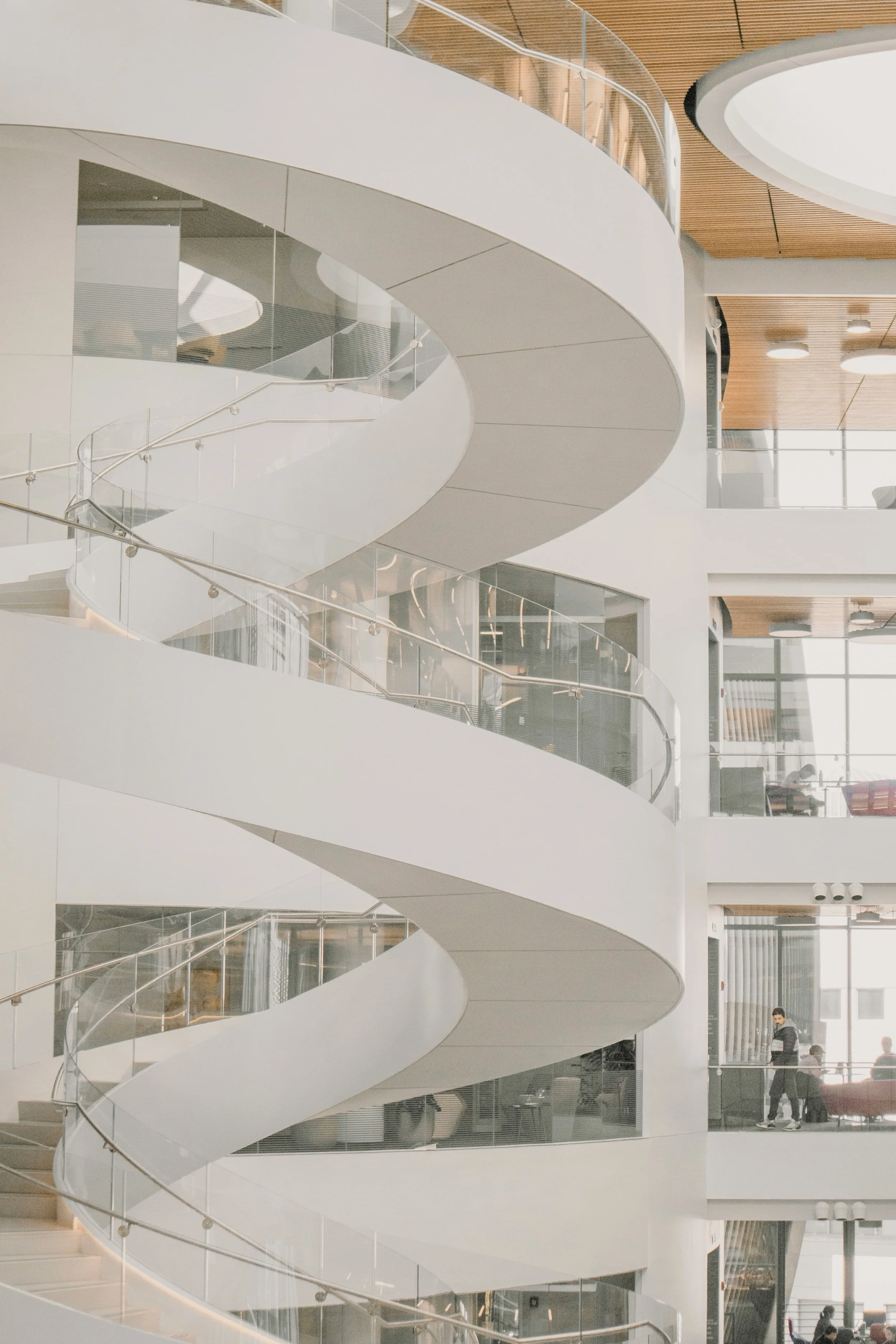 Modern building interior with white spiral staircase and glass railings.