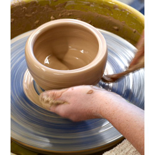 Person shaping a clay pot on a pottery wheel.