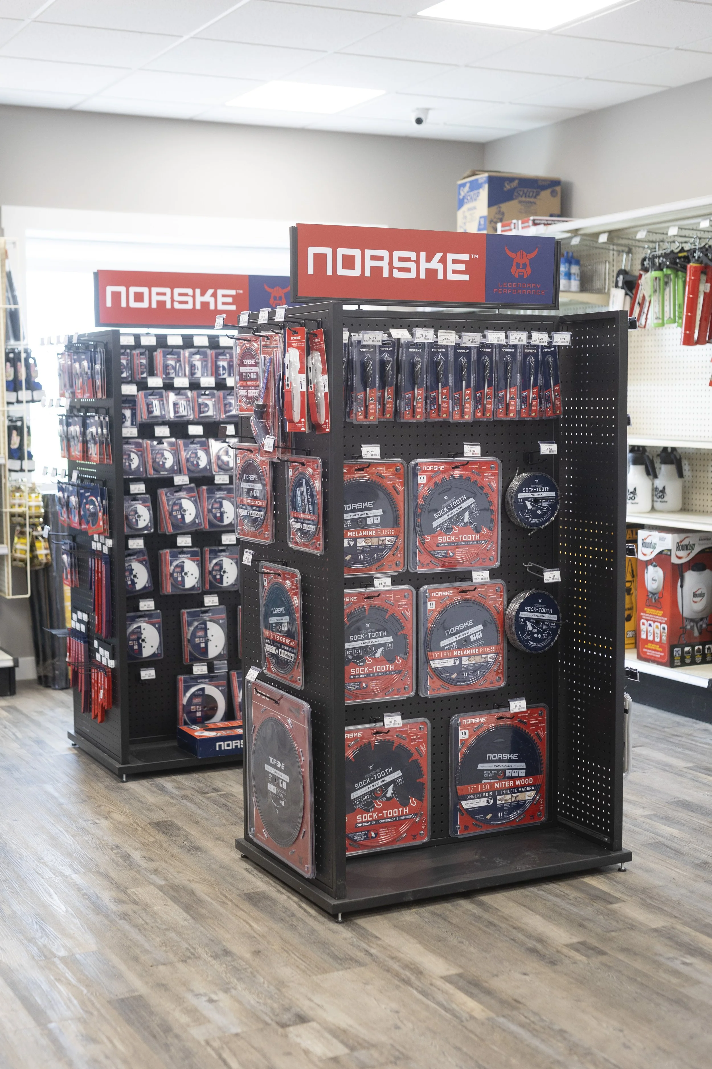 Product display of NORSKE chainsaws and related accessories on black pegboard shelves in a retail store.