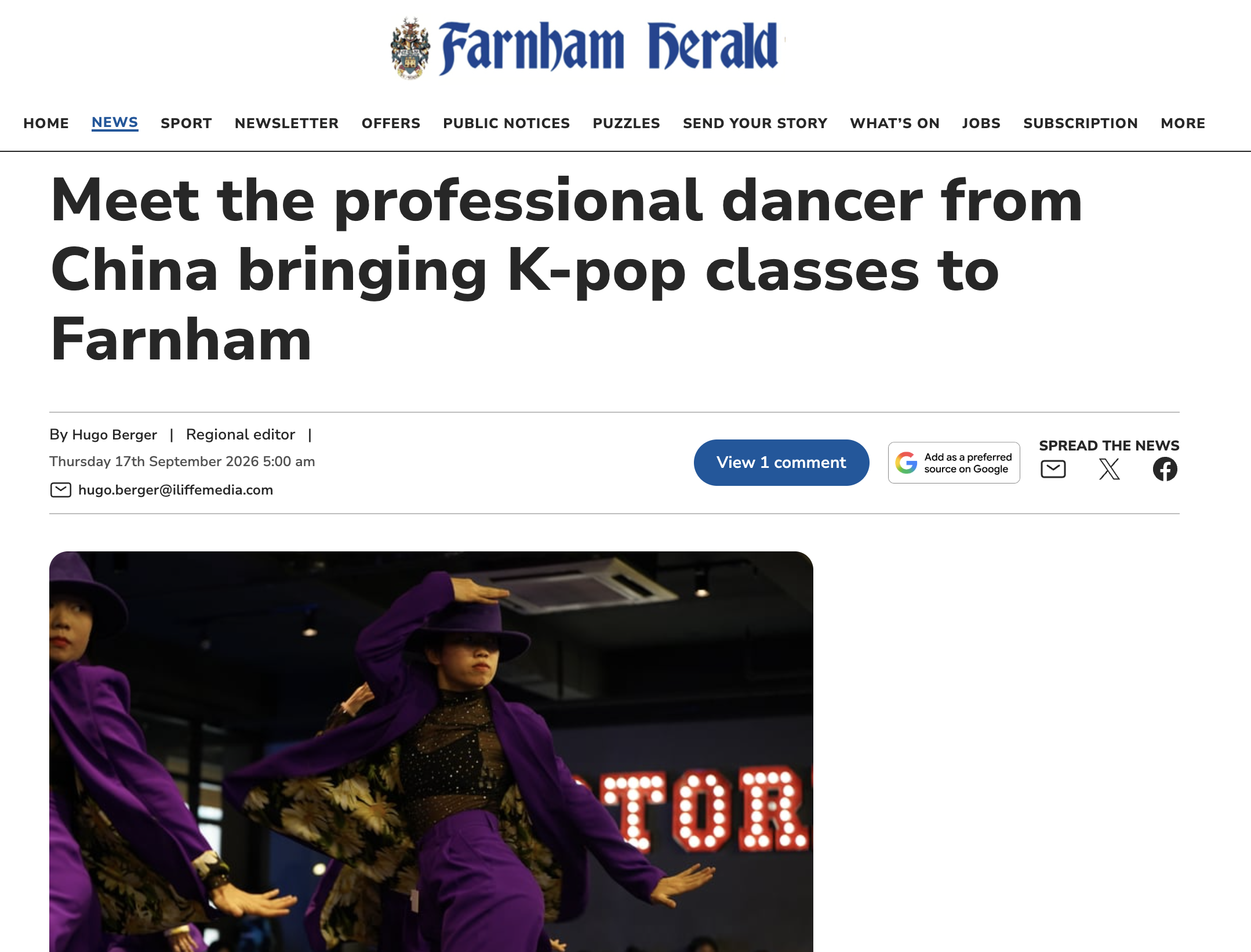 A group of performers on stage dressed in purple outfits and black hats, dancing with coordinated arm movements. The background features a red-lit sign with the word 'STOP' visible.