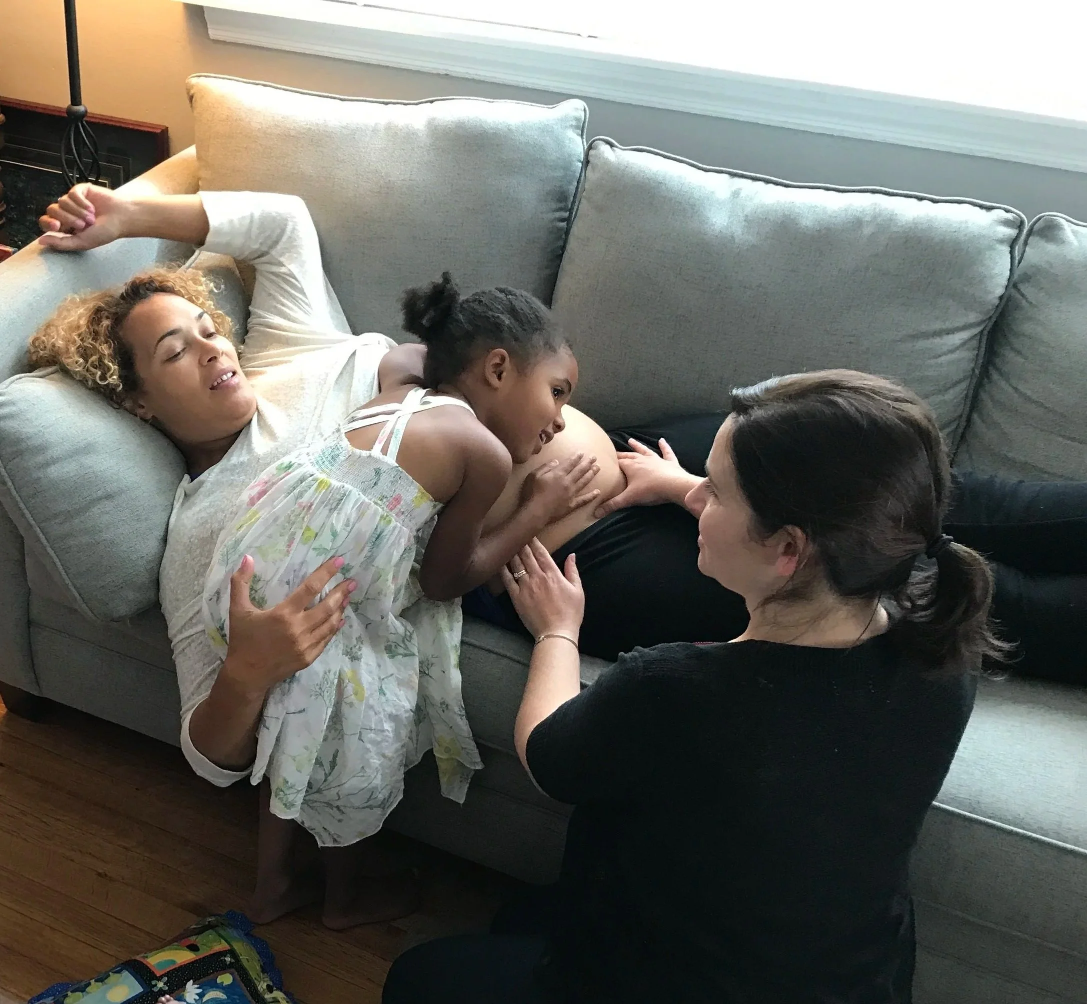 woman laying down with pregnant belly, child hugging her, woman checking pregnant belly