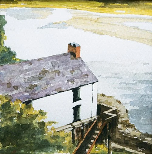 Watercolor painting of a white house with a gray roof and chimney, situated on a rocky shoreline with water in the background, surrounded by greenery in wales
