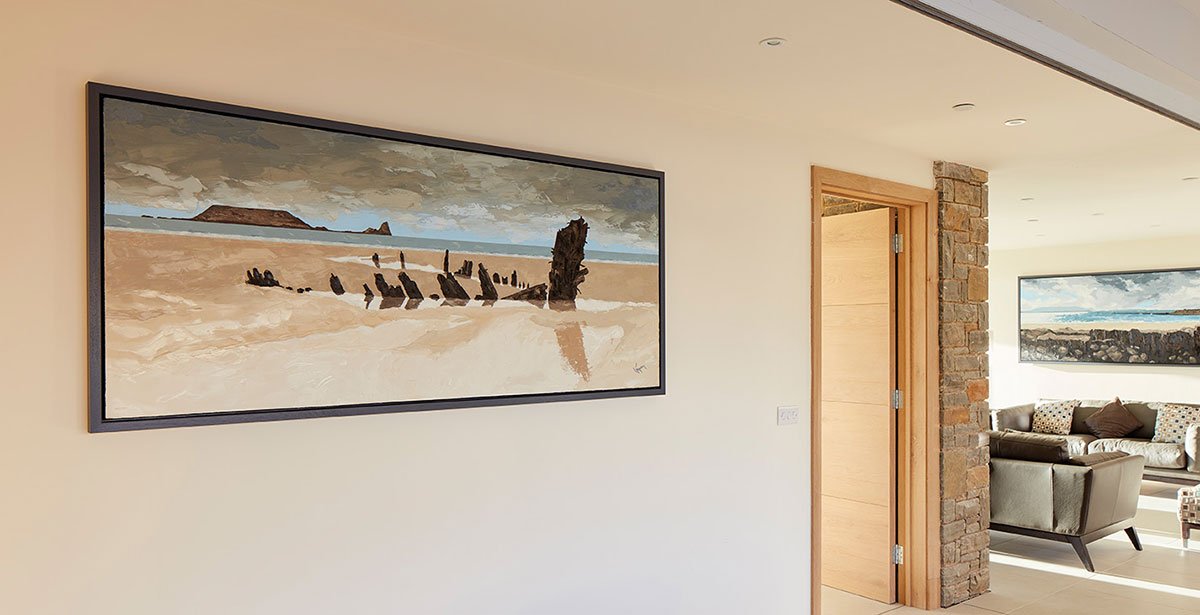 Living room with framed landscape painting of a beach scene on the wall and a seating area with chairs and a sofa.