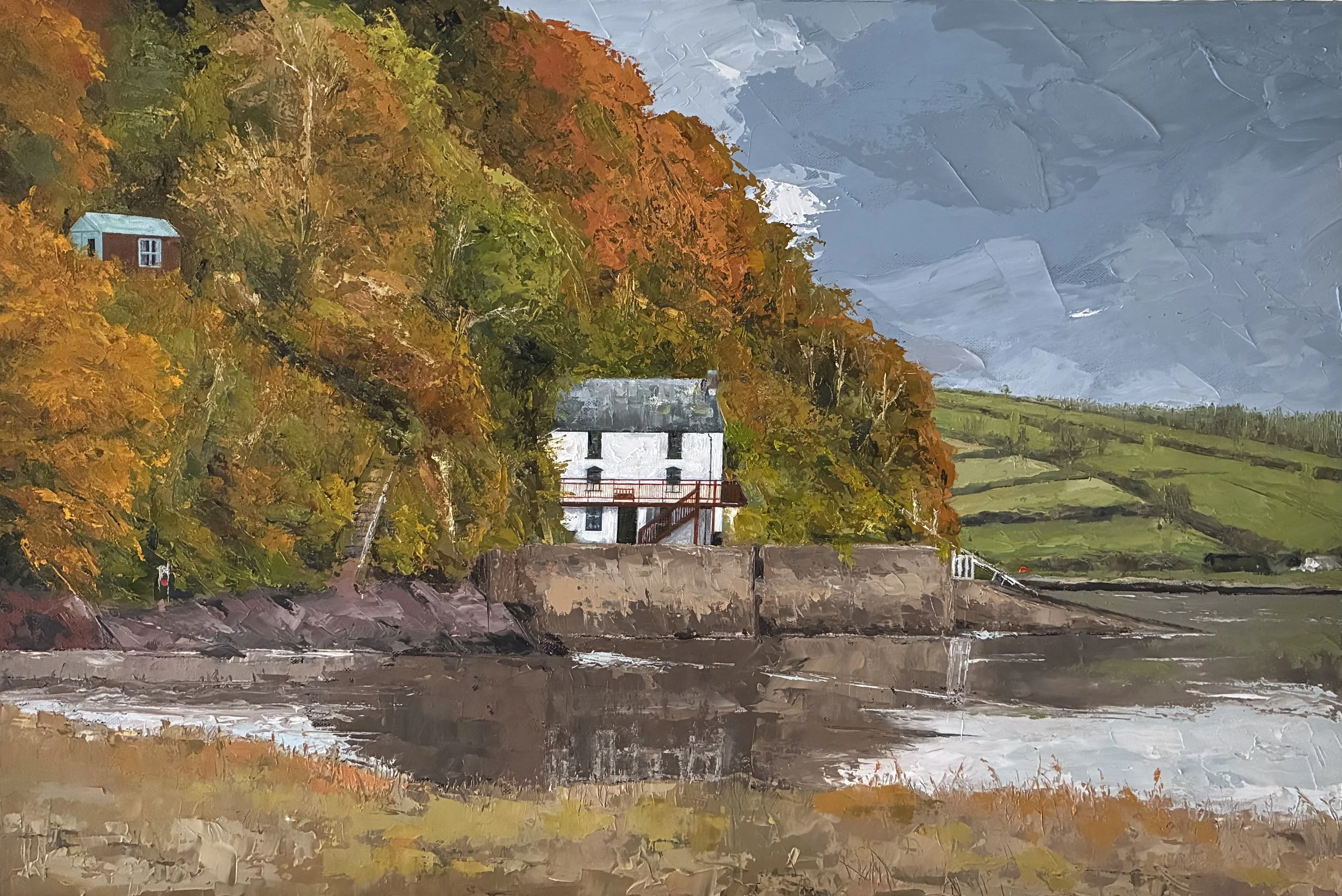 Painting of houses near a body of water, with trees with autumn foliage on a hillside and rolling green hills in the background, under a cloudy sky.